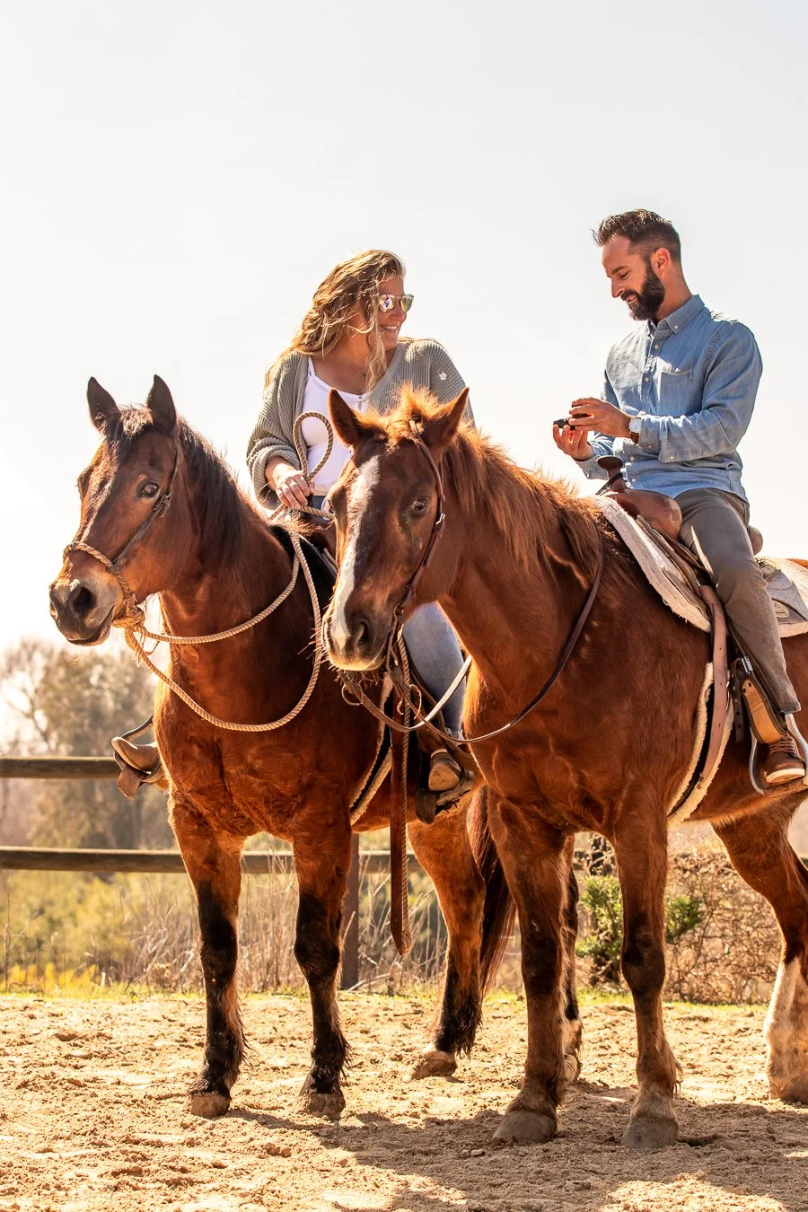 Two people riding horses and talking outdoors in sunnynweather.