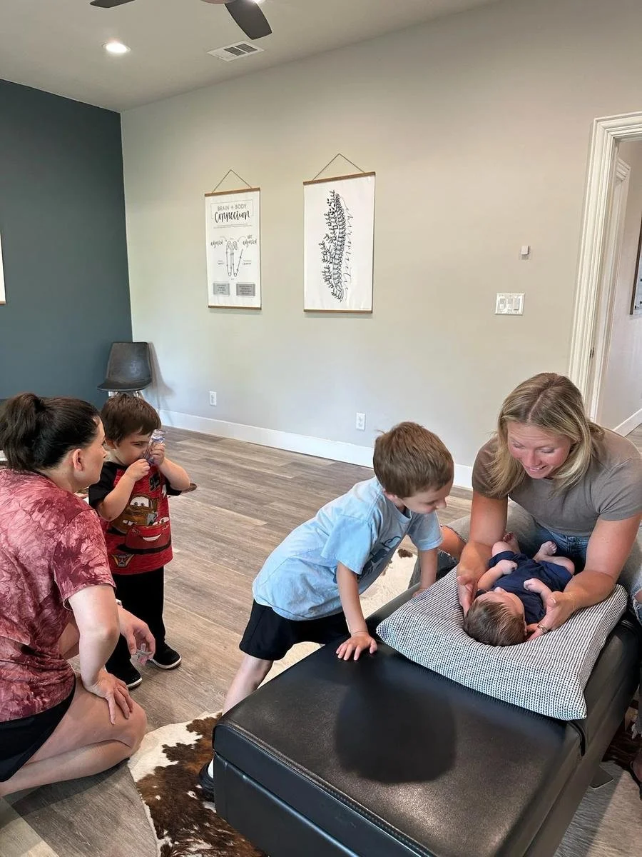 A complete family visit at Social House Chiropractic in Prosper, TX. Mom and siblings watch as Dr. Kara performs a gentle infant adjustment supporting nervous system development.