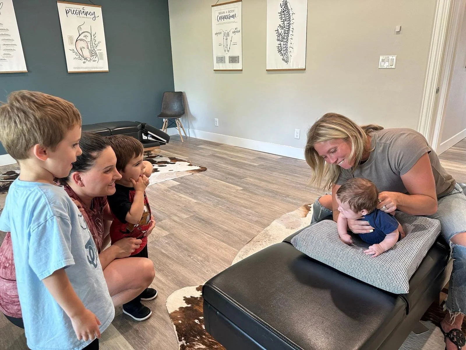 Dr. Kara Rodriguez performing a gentle infant chiropractic adjustment while older siblings observe at Social House Chiropractic in Prosper, TX. ICPA-trained pediatric chiropractic care for ADHD, focus, and nervous system support.