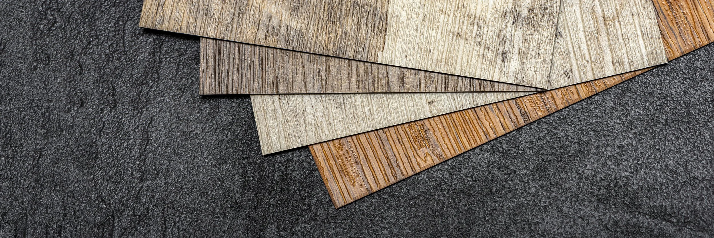 Collection of various luxury vinyl pl anks lvt flooring samples in different shades and textures, fanned out on a wooden surface.