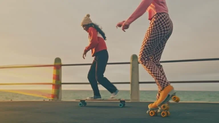 Two people skateboarding along a seaside promenade during sunset.