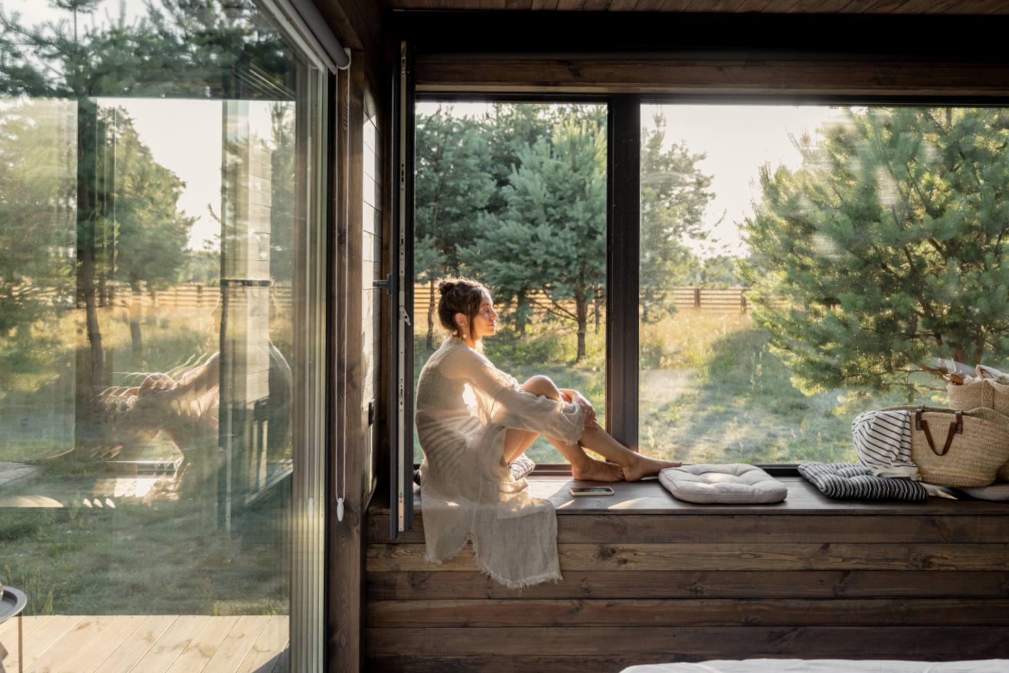 A woman with long, curly hair standing outdoors in sunlight, wearing a white crocheted shawl with fringe, arms outstretched, and eyes closed.