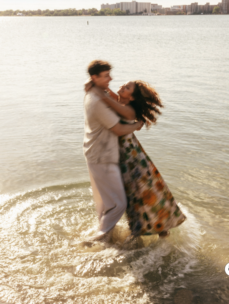 A man and a young girl lying on a bed, with the girl holding a closed book, both looking happily at each other.