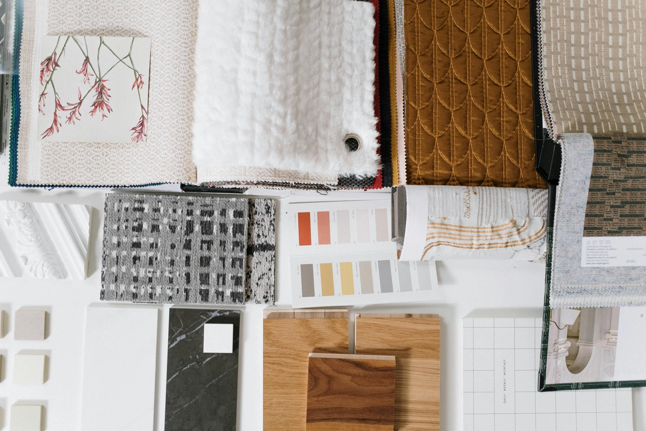 Échantillons de tissus, de matériaux pour décoration intérieure comme des tapis, des échantillons de bois, des couleurs de peinture, et des éléments pour la décoration.