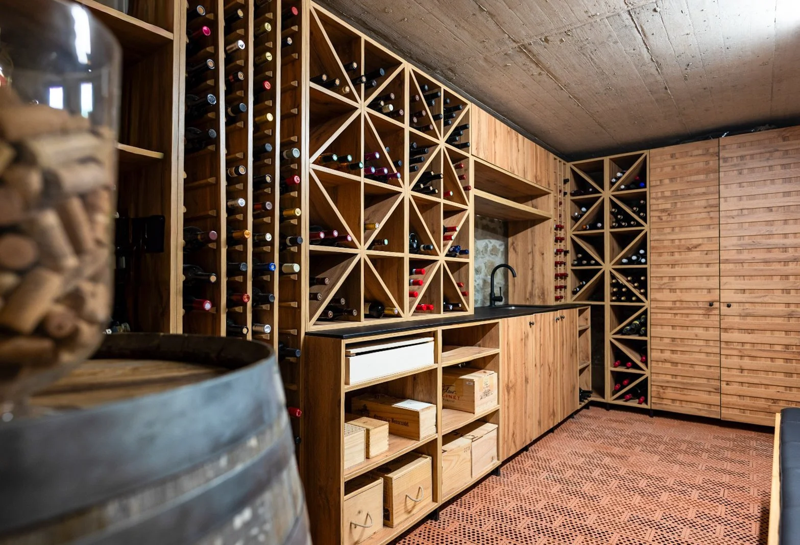 Cave à vin avec étagères en bois remplies de bouteilles de vin, évier noir et rangement en bois.