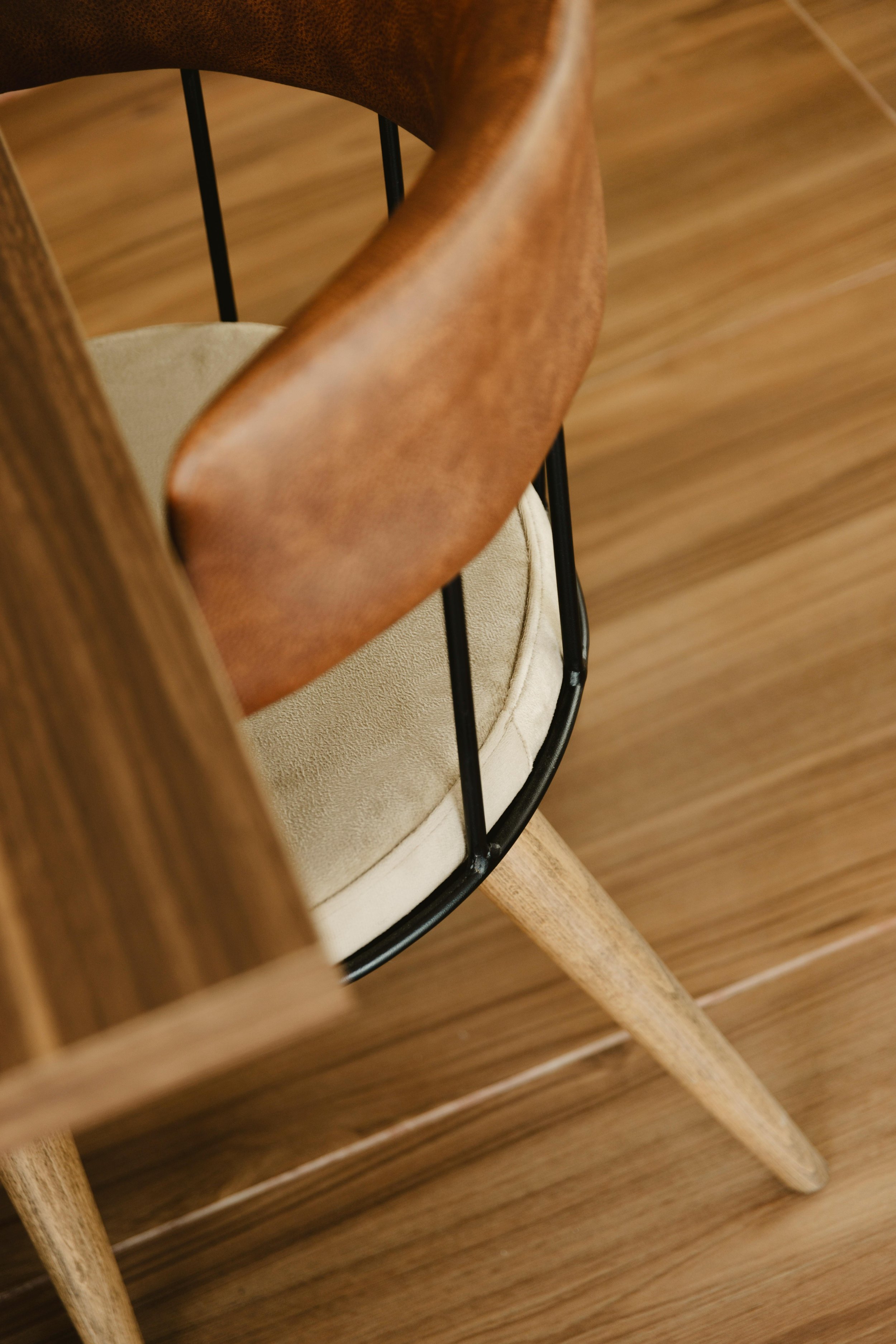 Vue rapprochée d'une chaise en bois avec un coussin beige et un dossier en bois courbé, vue partielle dans une pièce avec un sol en bois.