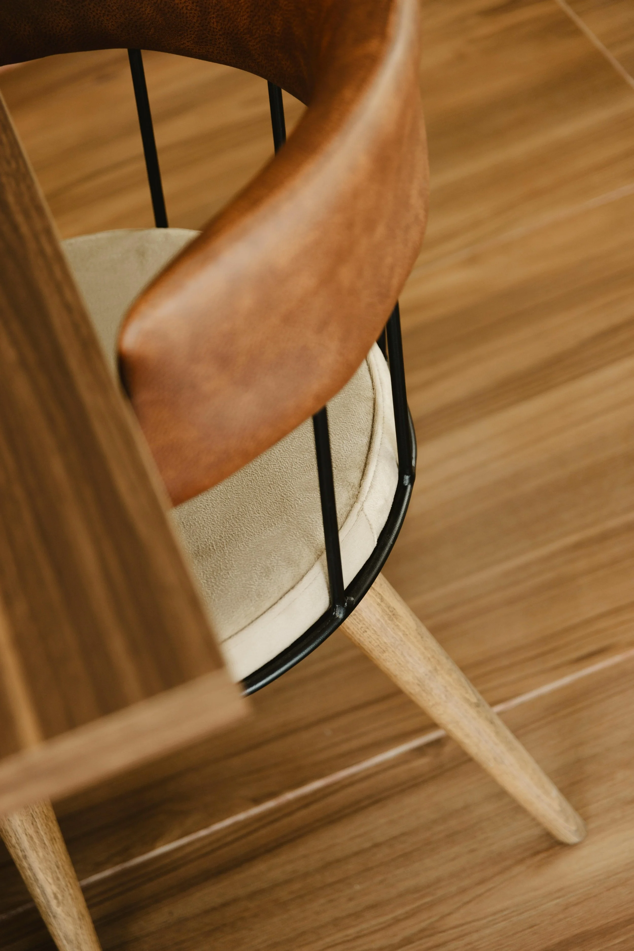 Vue rapprochée d'une chaise en bois avec un coussin beige et un dossier en bois courbé, vue partielle dans une pièce avec un sol en bois.