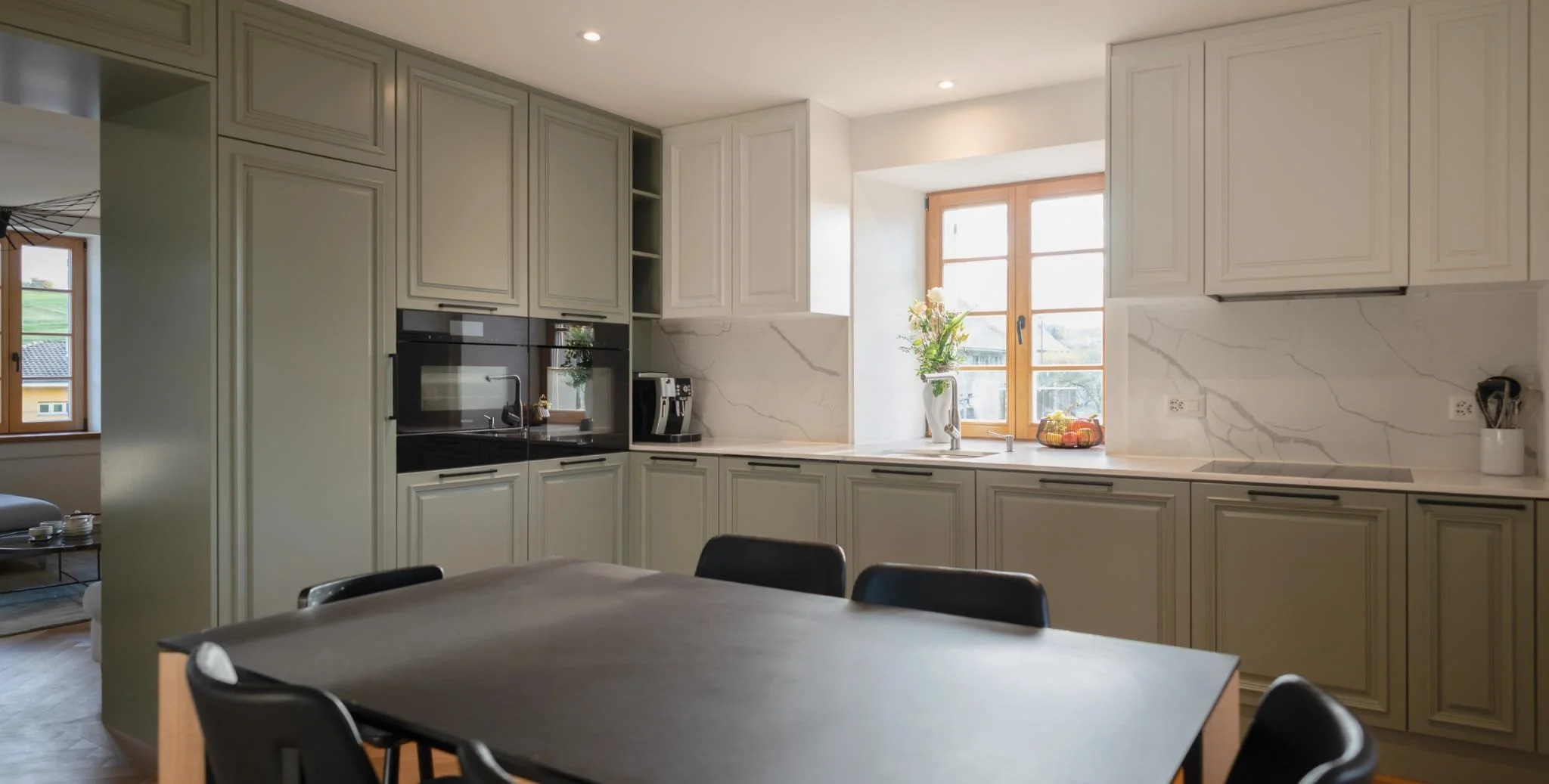 Cuisine moderne avec fenêtres, meubles blancs, marbre sur les murs, planche de cuisson et évier, table noire avec chaises.