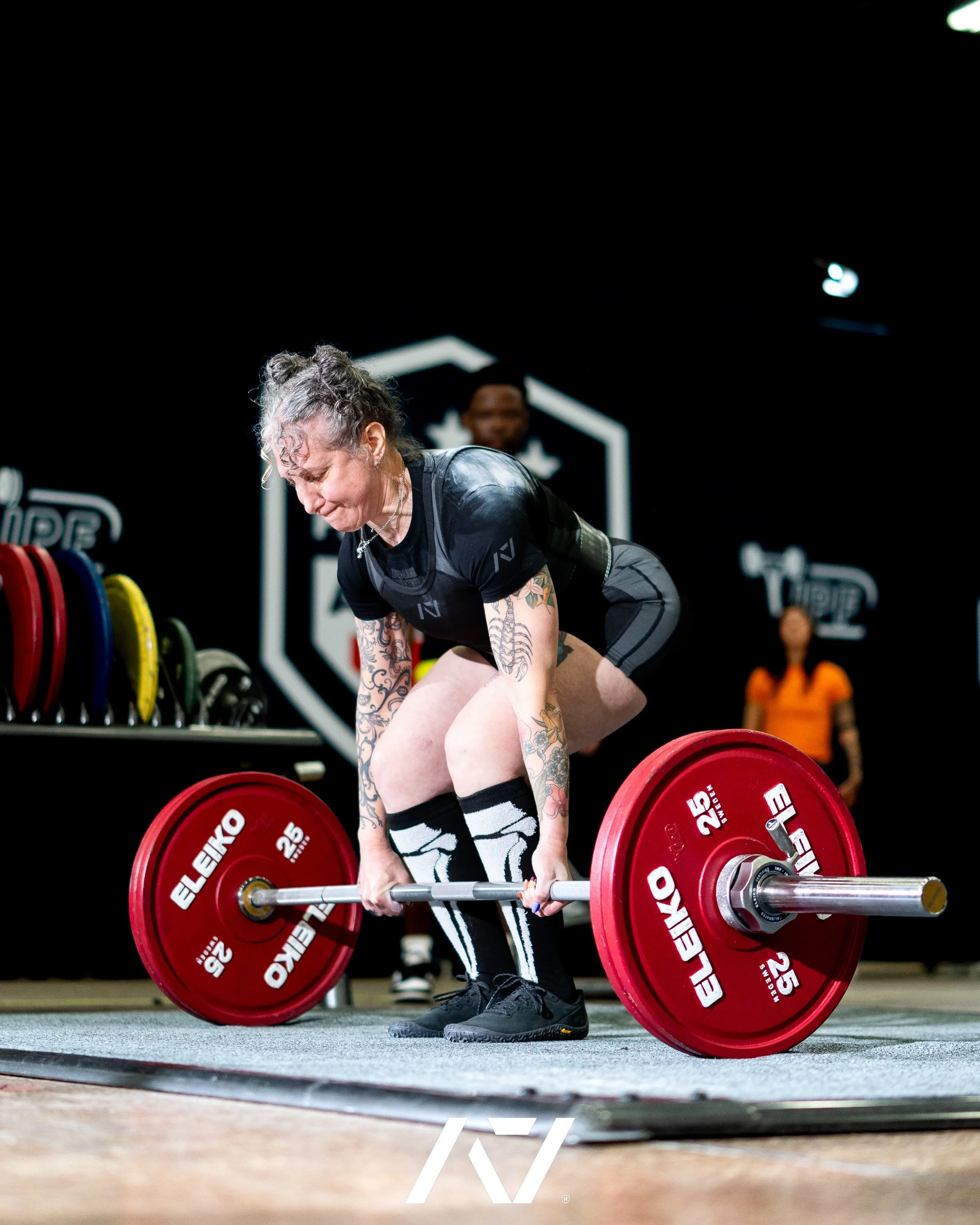 Close-up of an athlete gripping a barbell loaded with red weight plates, preparing for a strength training lift in a gym.