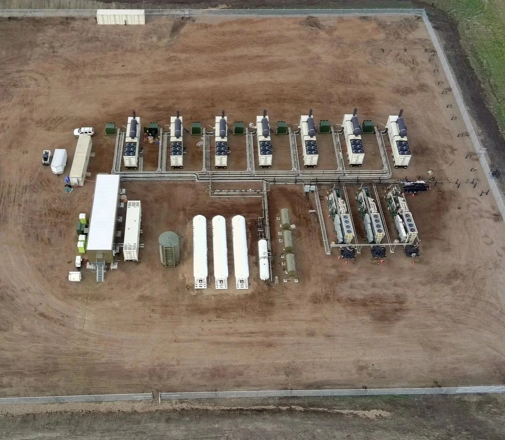 Aerial view of a microgrid with portable generators and gas processing equipment on a large cleared area of land.
