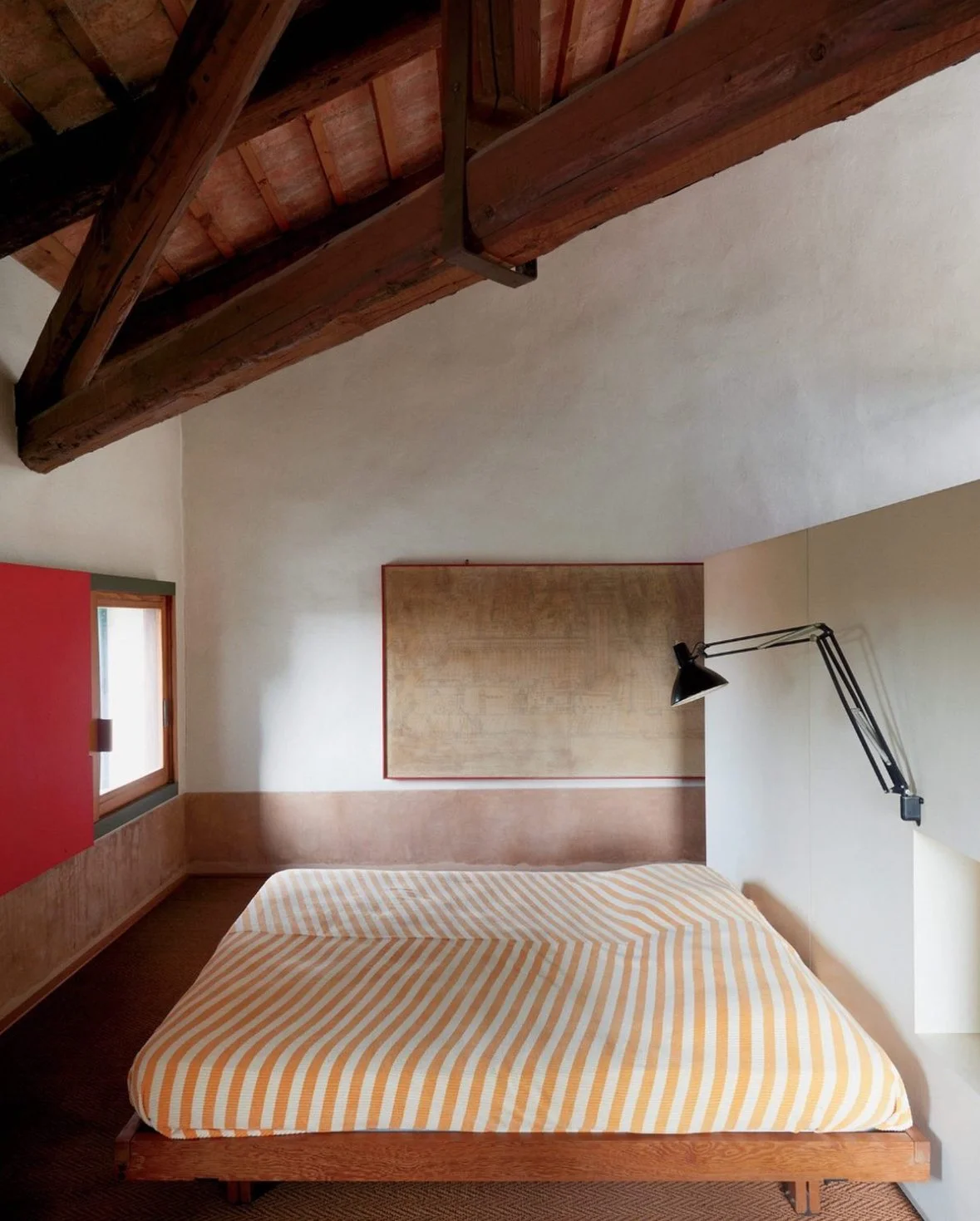 Bedroom with a single bed, orange and white striped bedding, wooden headboard, black adjustable wall lamp, small window, and wooden ceiling beam.