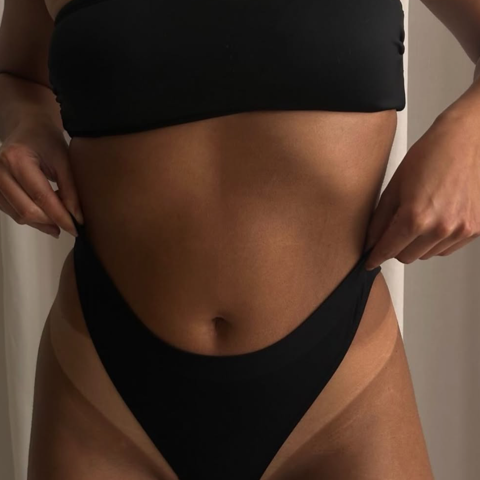 Close-up of a woman adjusting her black underwear, showing her midsection and belly button.