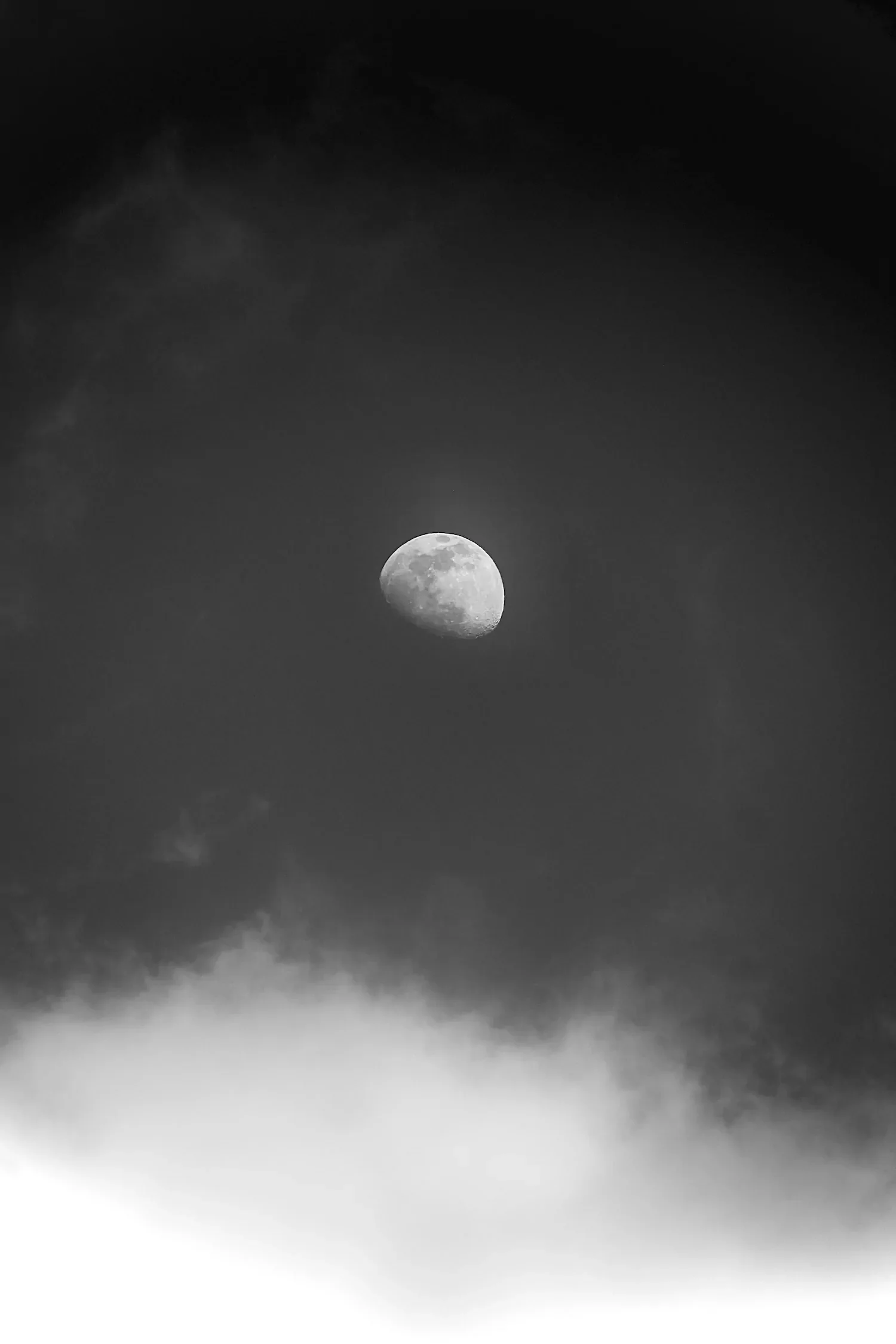 A black and white photograph of the moon in a dark sky with white clouds beneath.