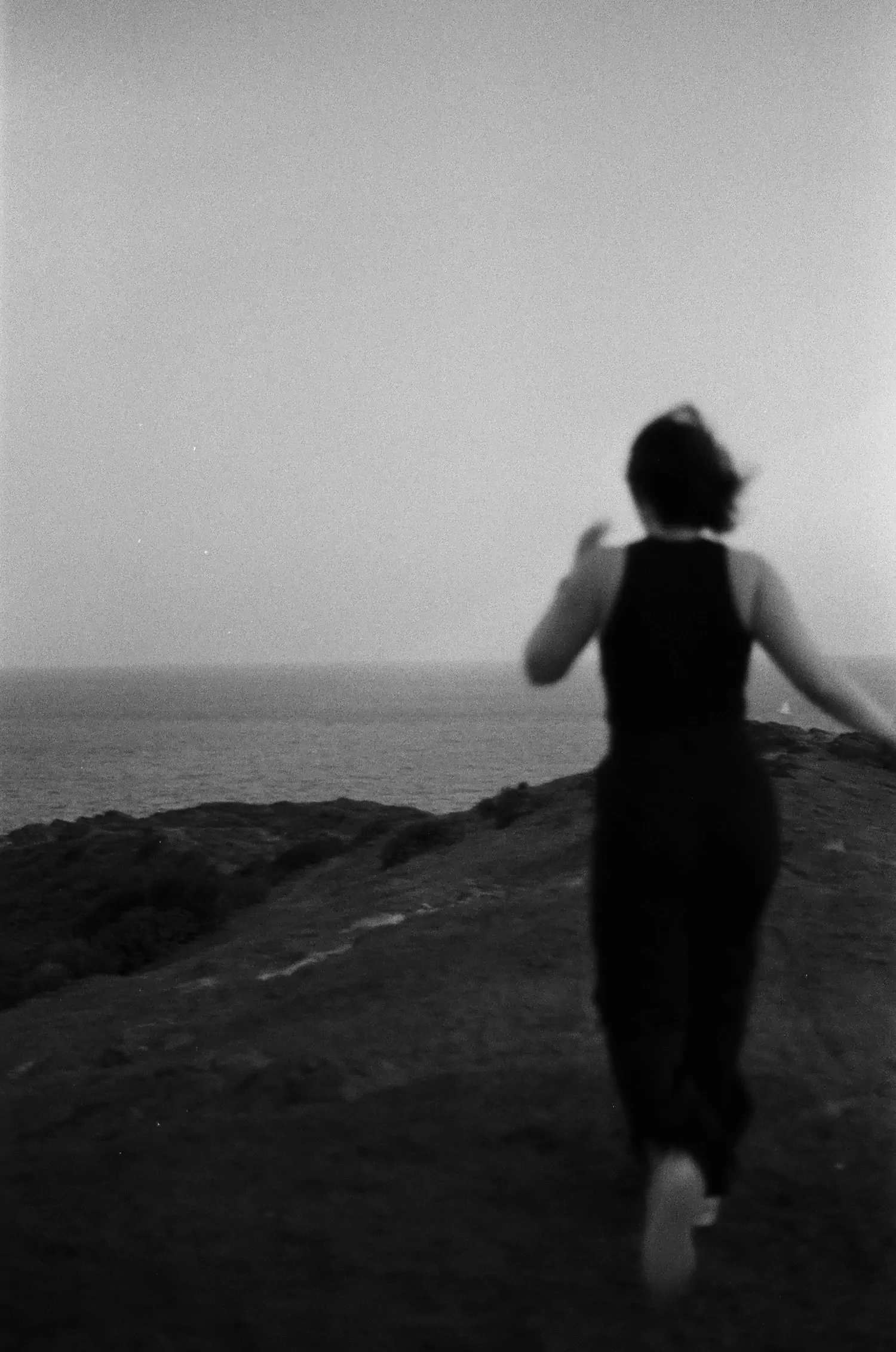 Black and white photograph of woman running toward a shoreline.