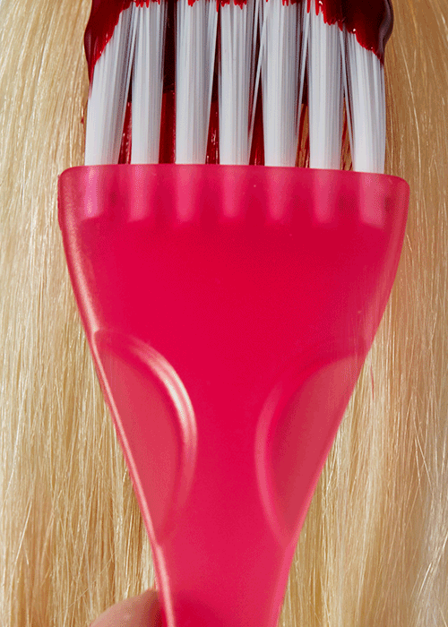 Close-up of a pink spatula lifting raw white and red striped candies from a wooden surface.