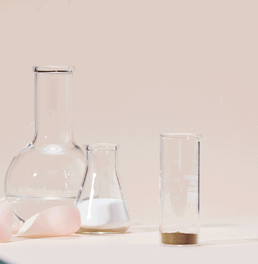 Close-up of laboratory glassware including a round-bottom flask, Erlenmeyer flask, and graduated cylinder, with a white powder or substance at the bottom of the graduated cylinder.