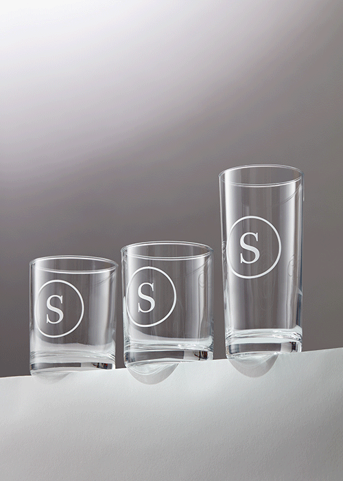 Three clear glasses with white circle and 'S' logo, arranged from shortest to tallest, on a white surface against a gradient gray background.