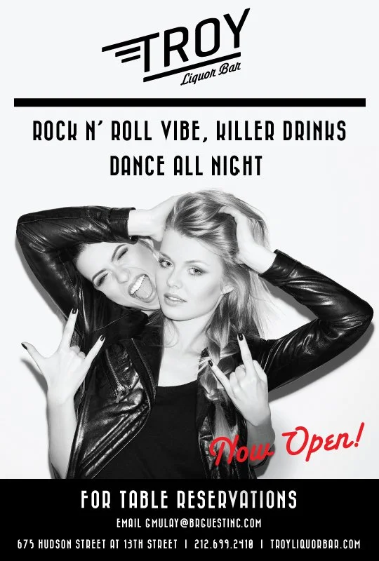 A promotional poster for Troy Liquor Bar featuring two women dressed in black leather jackets making rock and roll hand gestures, with one woman showing her tongue and the other looking serious. The poster highlights the bar's opening, musical vibe,