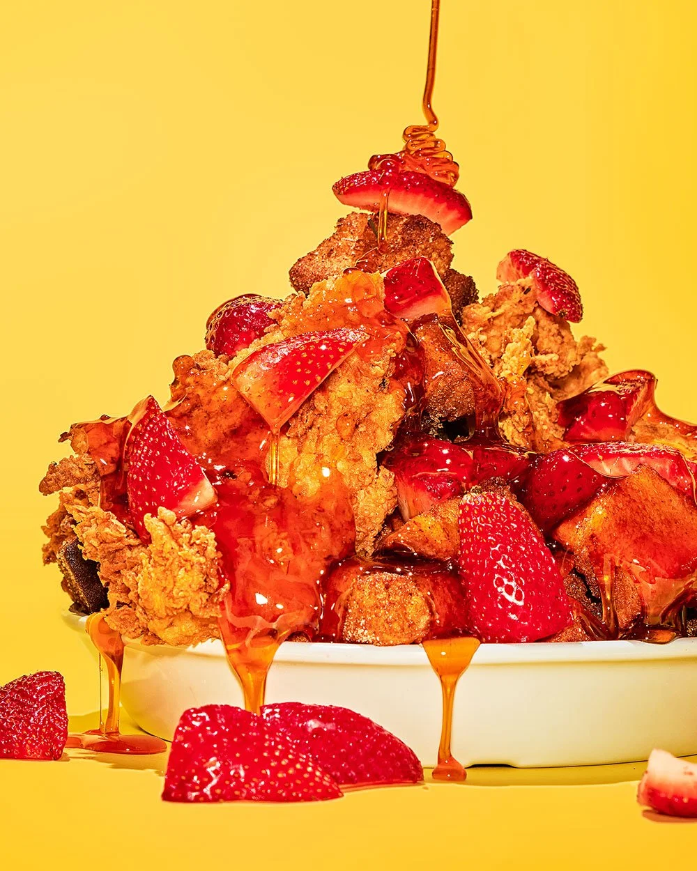Close-up of a bowl filled with fried chicken topped with fresh strawberries and drizzled with strawberry syrup on a yellow background.
