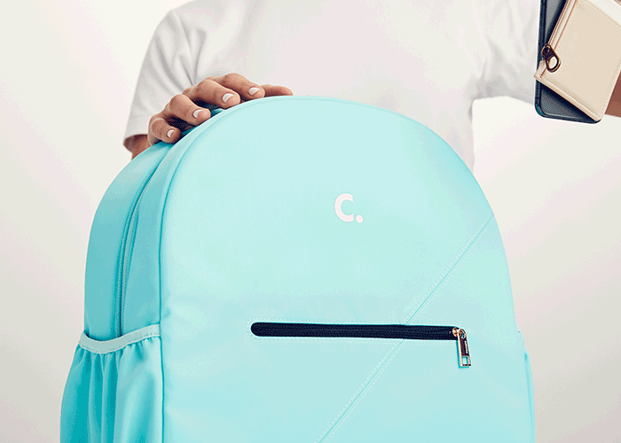 A person holding a light blue backpack with one hand, showing a zipper pocket, and holding a notebook in the other hand.