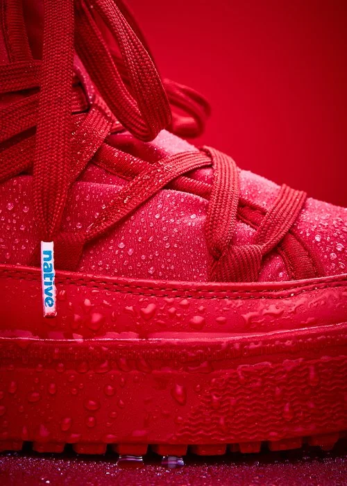 Close-up of a red sneaker with water droplets and water droplets on the sole, featuring a blue and white "native" tag.
