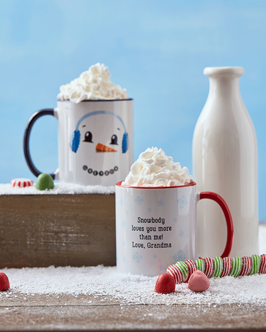 Two mugs of whipped cream on a wooden surface with snowman and Christmas-themed decorations, a white vase, and candy canes, with a snow-themed background.