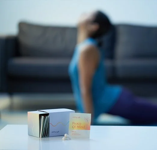 A woman practicing yoga or meditation at home, with a focus on a box of relaxation or meditation products on a table in the foreground.