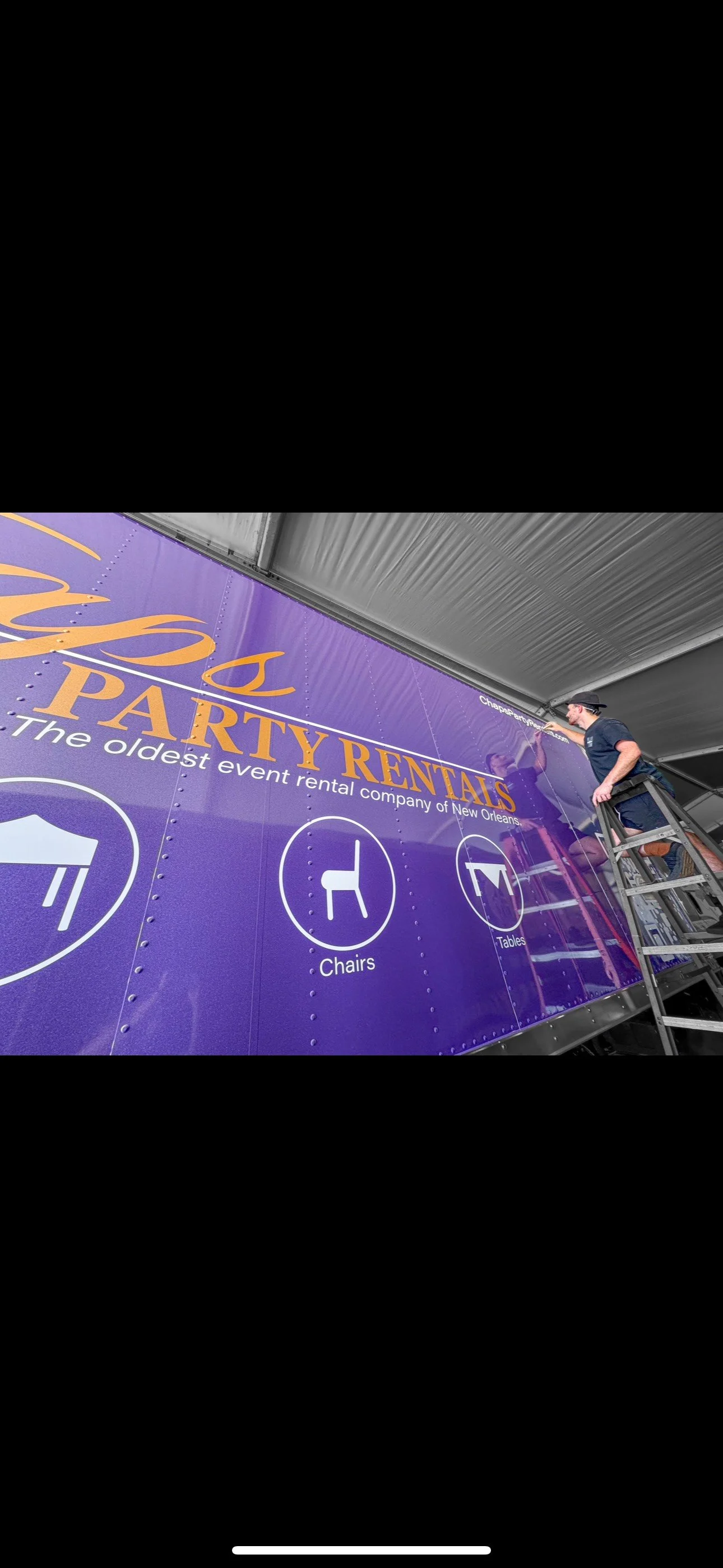 A person on a ladder cleaning a large purple party rental trailer with the text 'Party Rentals' and icons for chairs and tables.