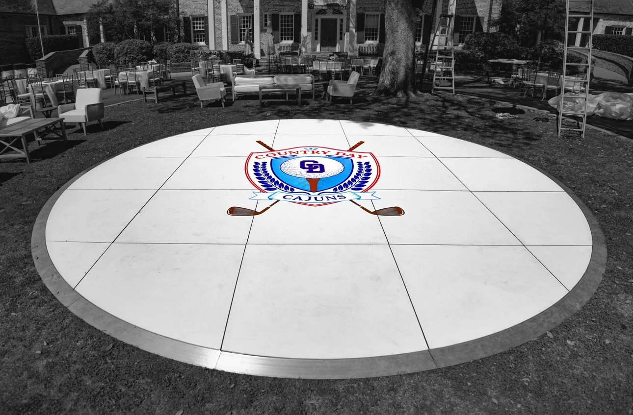 Circular outdoor floor with a logo of the LSU Cajuns in the center, featuring crossed hockey sticks underneath, surrounded by outdoor furniture and a large tree in the background.