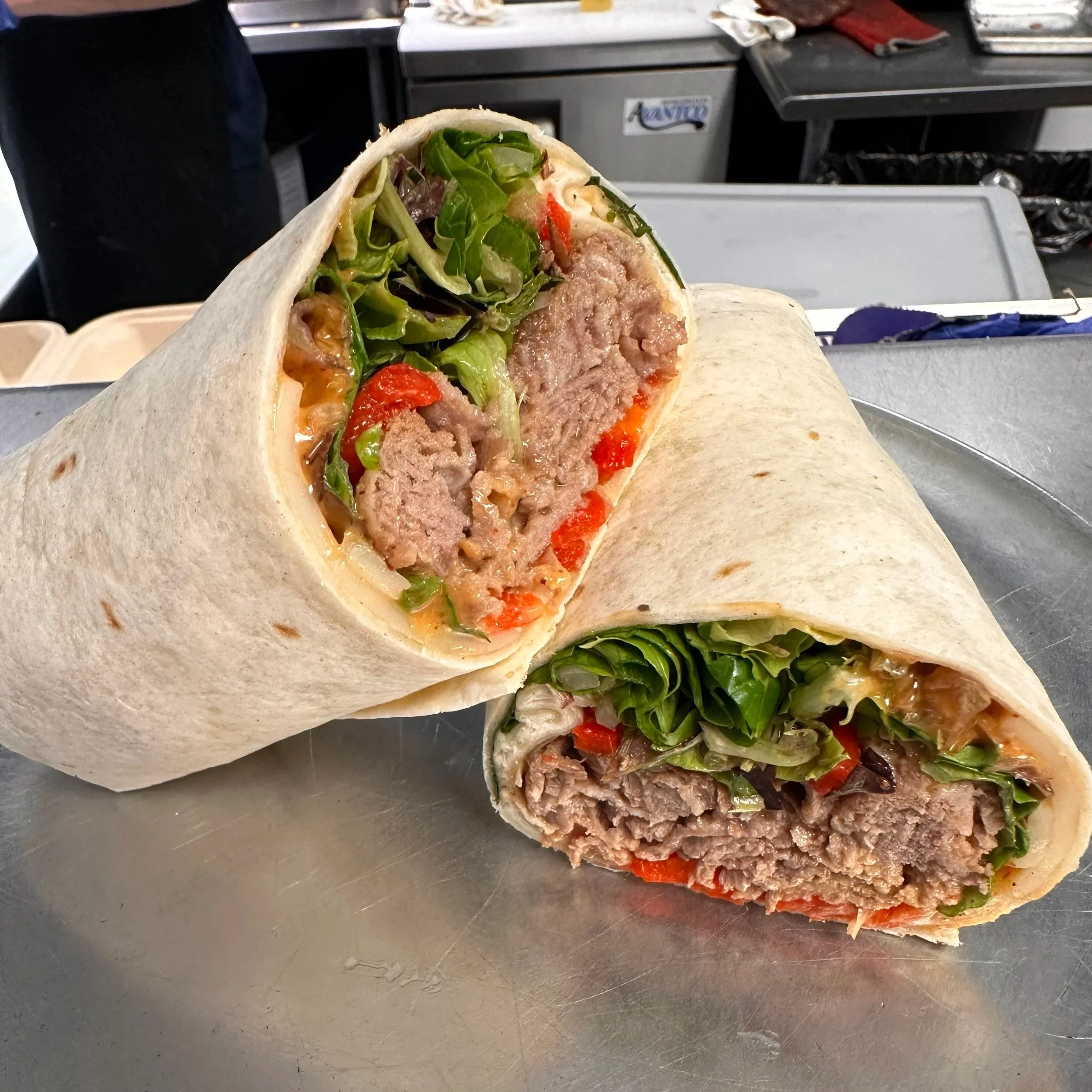 Cross-section of a wrapped burrito with beef, lettuce, tomatoes, and sauce on a metal surface.