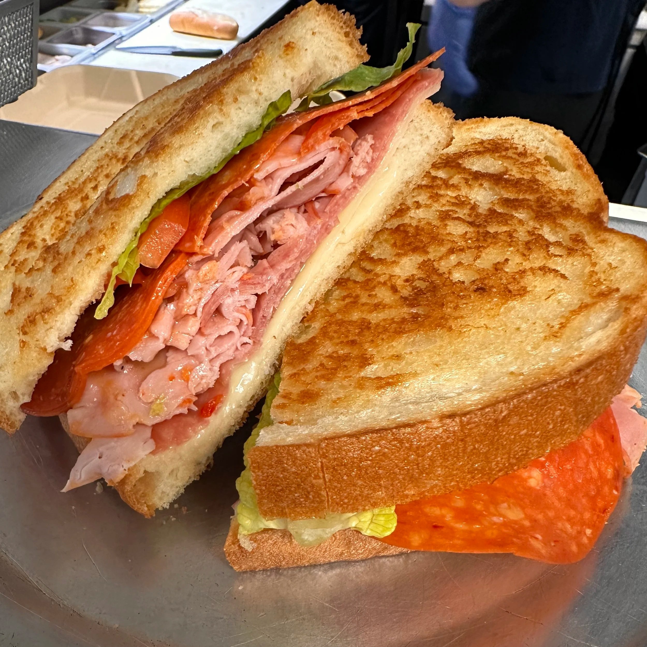 Close-up of a large sandwich with toasted bread, layers of sliced turkey and ham, lettuce, tomato, and cheese.