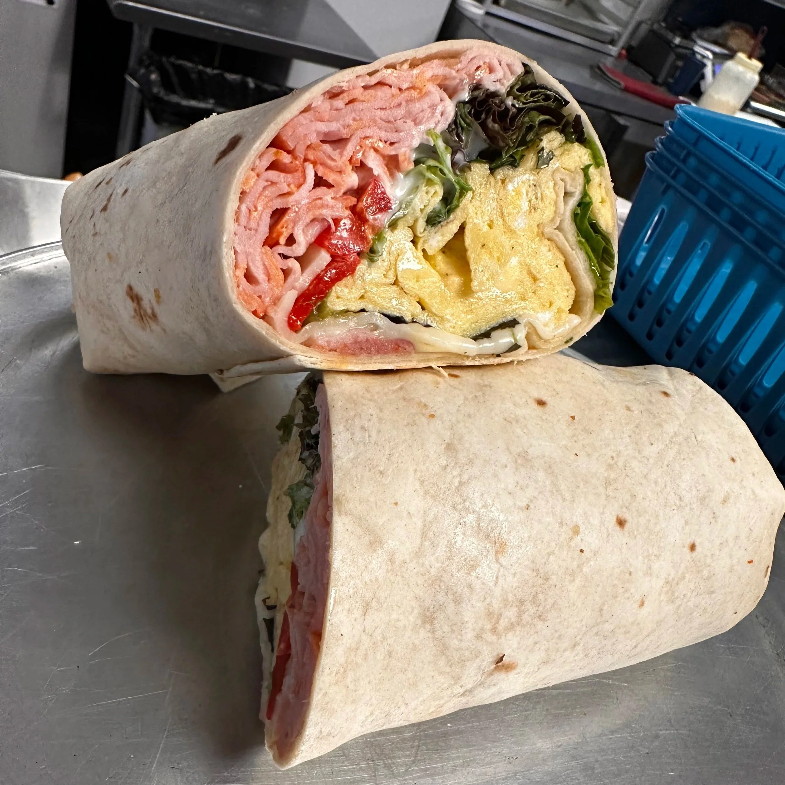 A cut-open wrap sandwich showing lettuce, tomato, eggs, ham, and cheese.