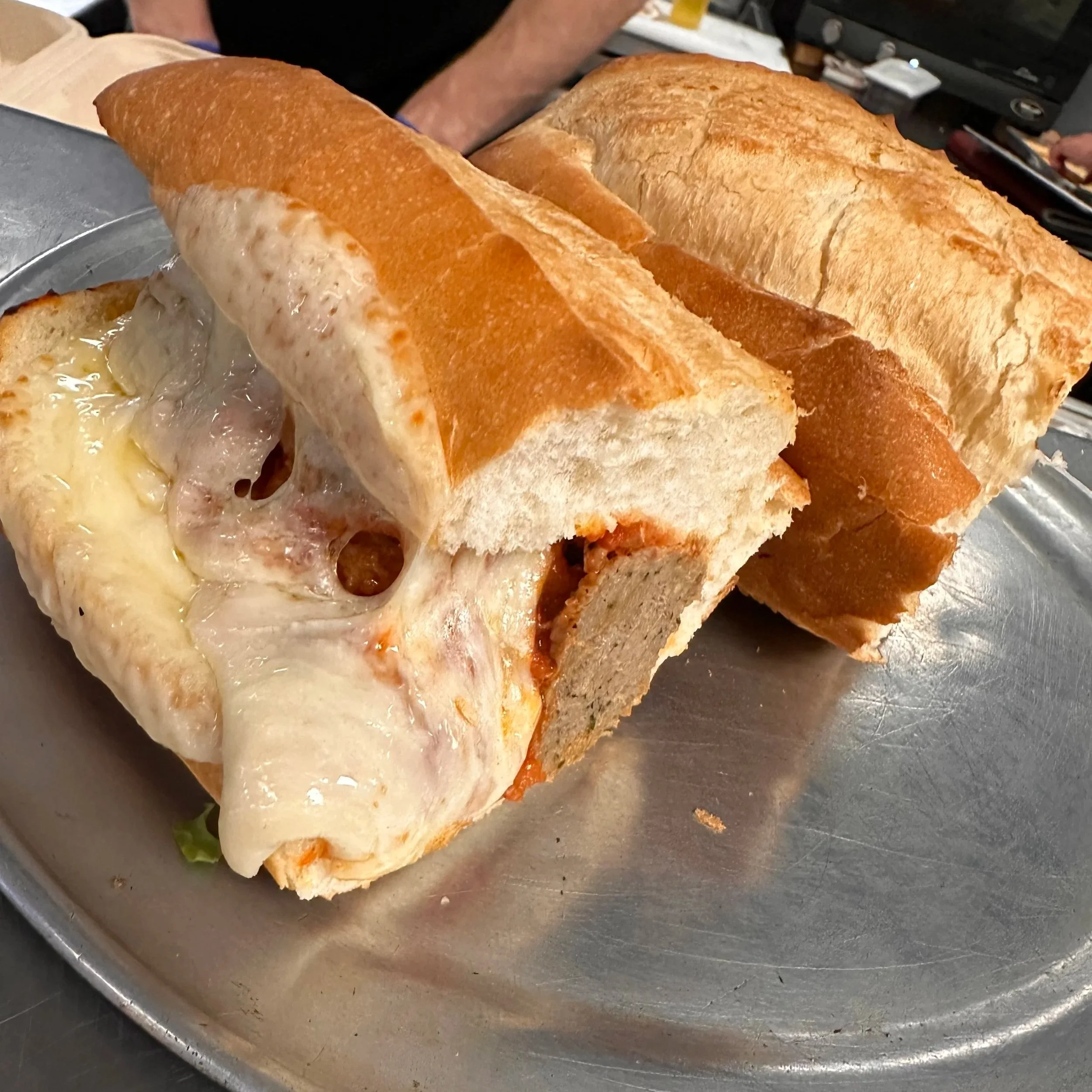 A large sub sandwich with melted cheese, slices of meat, and toasted bread, served on a metal tray.