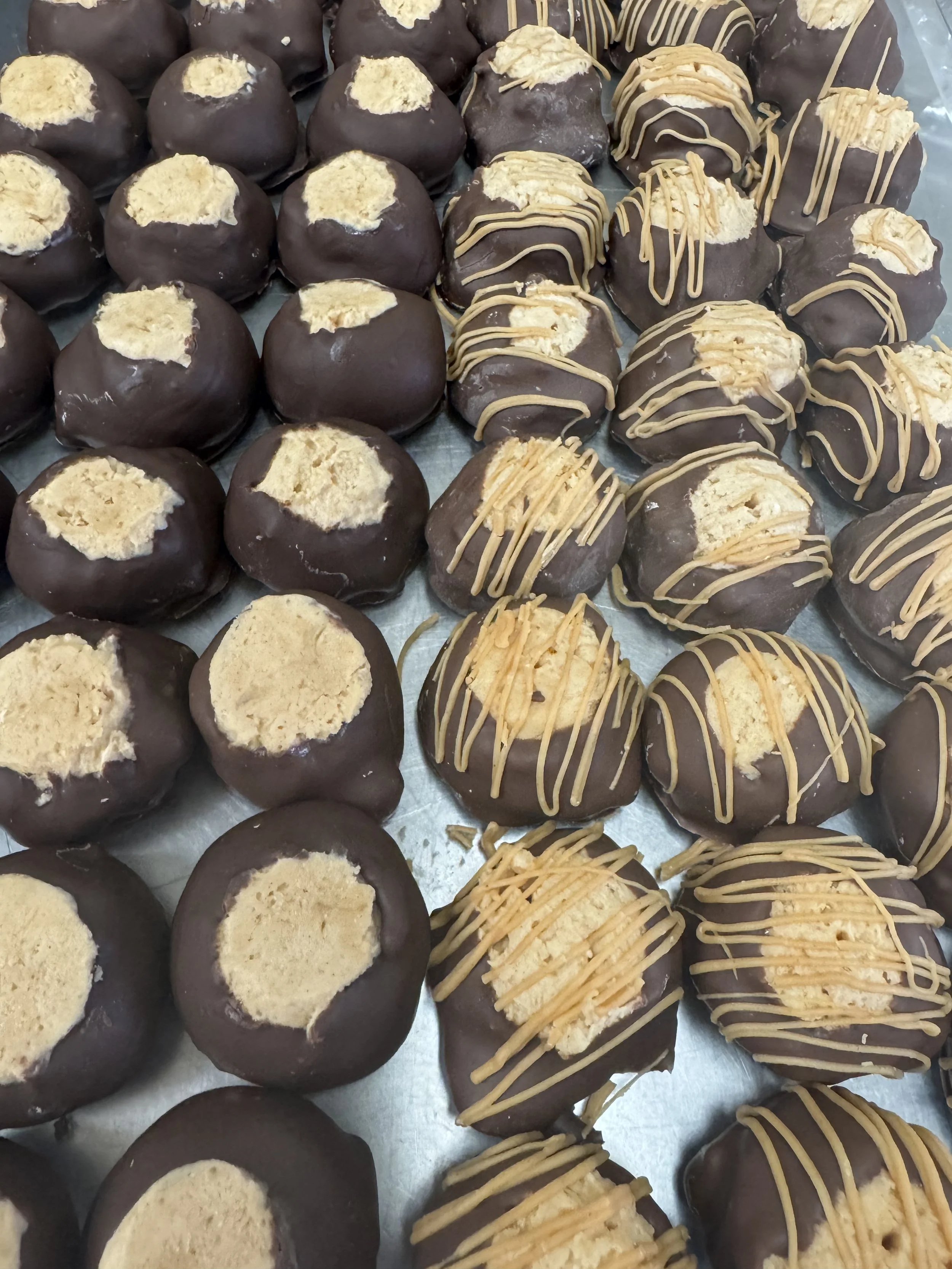 Arrangement of chocolate-covered cookies with some topped with yellow drizzle and others with a light-colored filling visible.
