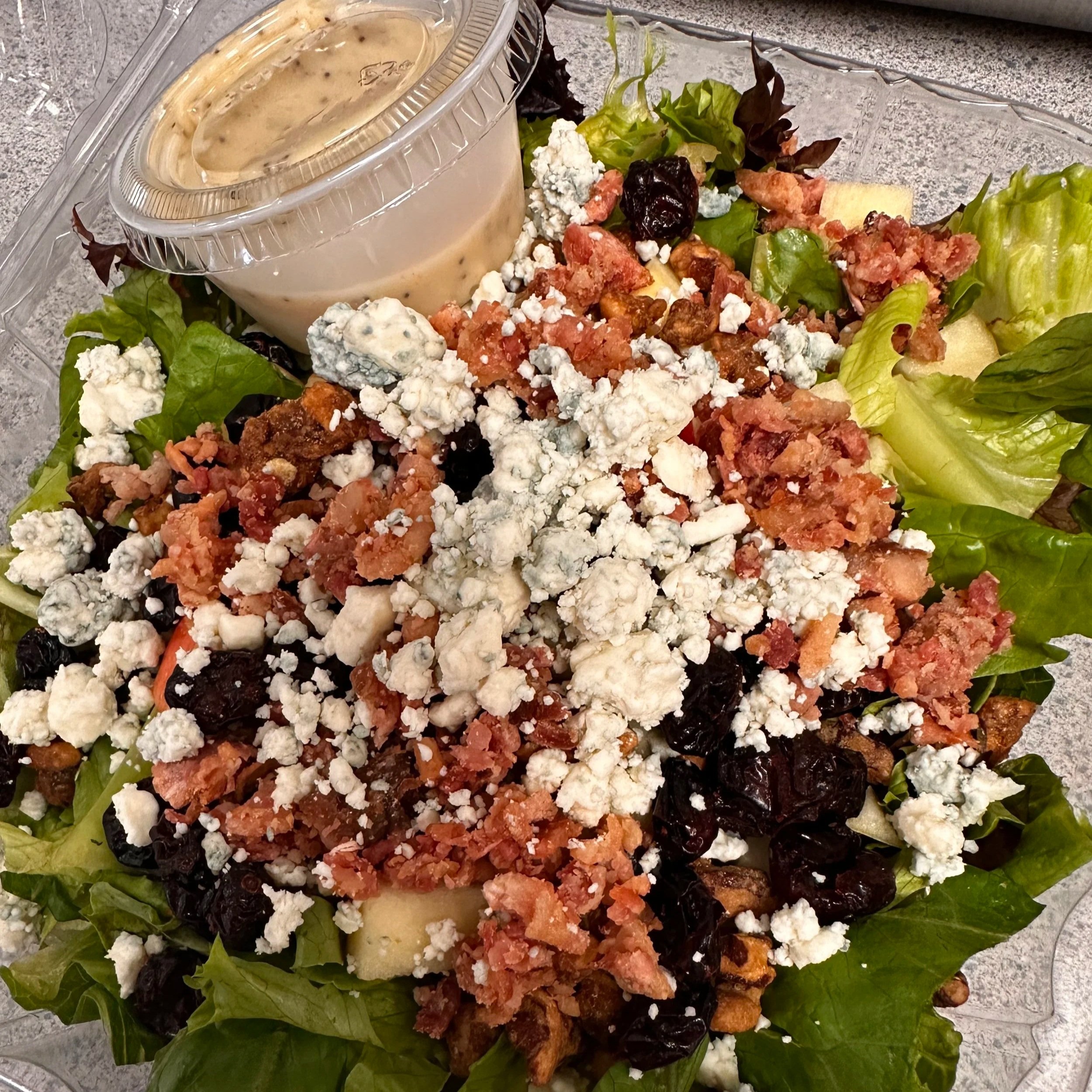 Salad with lettuce, blueberries, walnuts, crumbled blue cheese, and bacon bits, served with a container of ranch dressing.