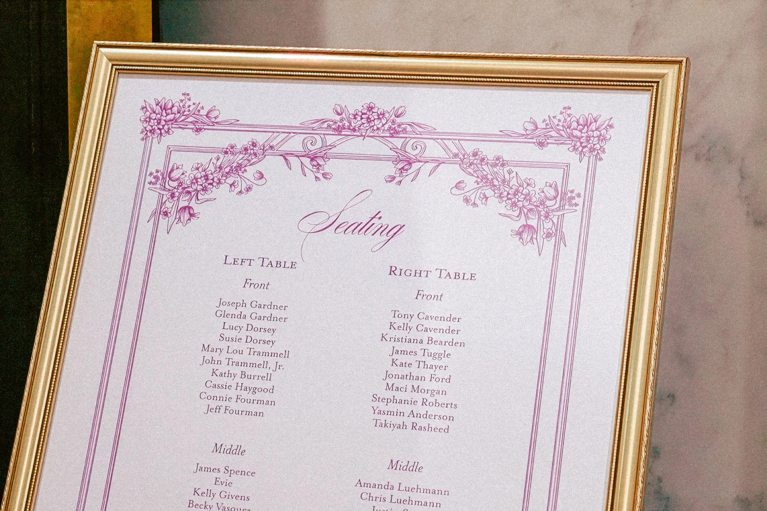 A framed seating chart for an event, featuring an ornate floral design in purple on a white background, with list of guest names under categories for left, right, middle, and other seating sections.