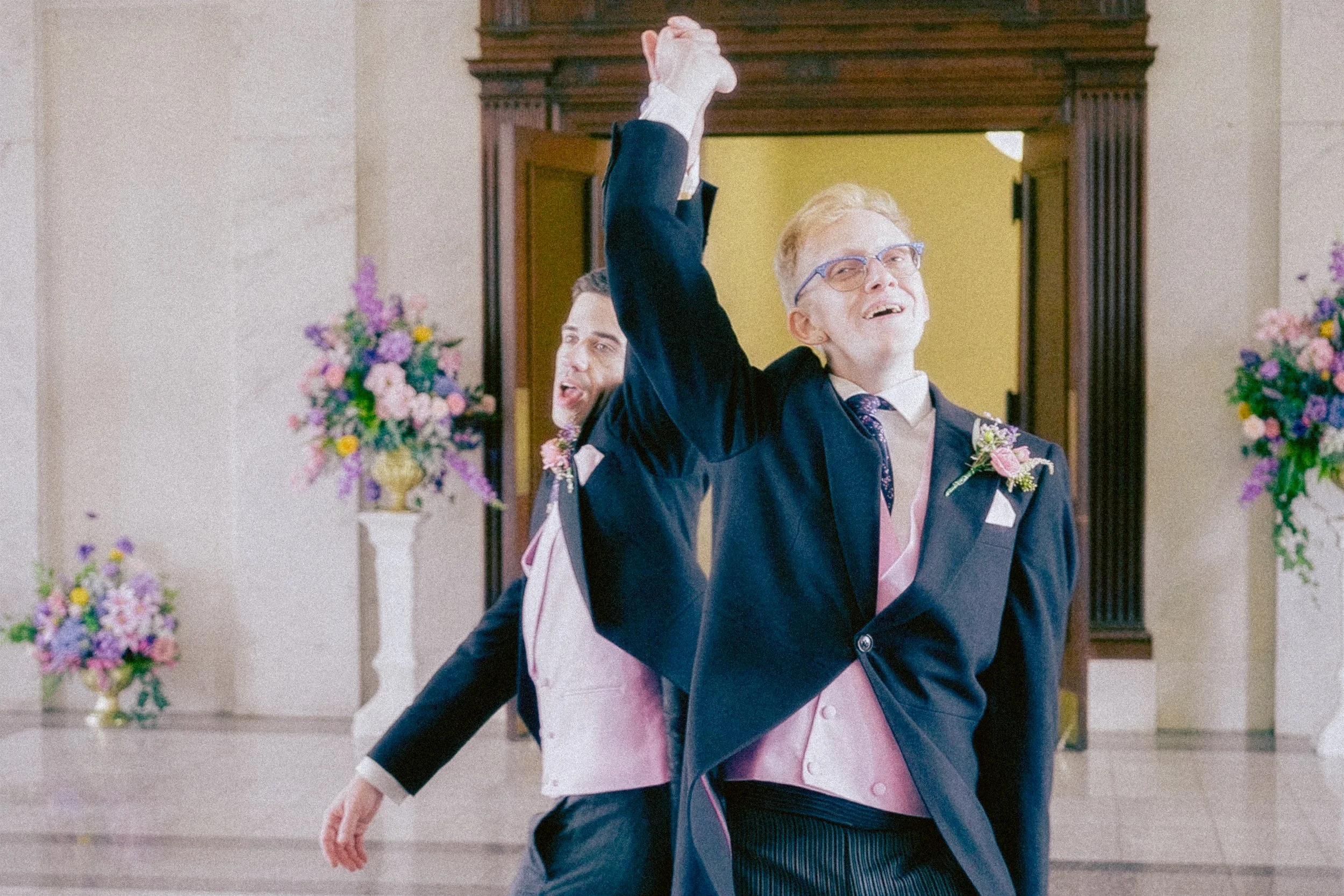 Two men in suits enjoying a dance in a decorated indoor space with flower arrangements.