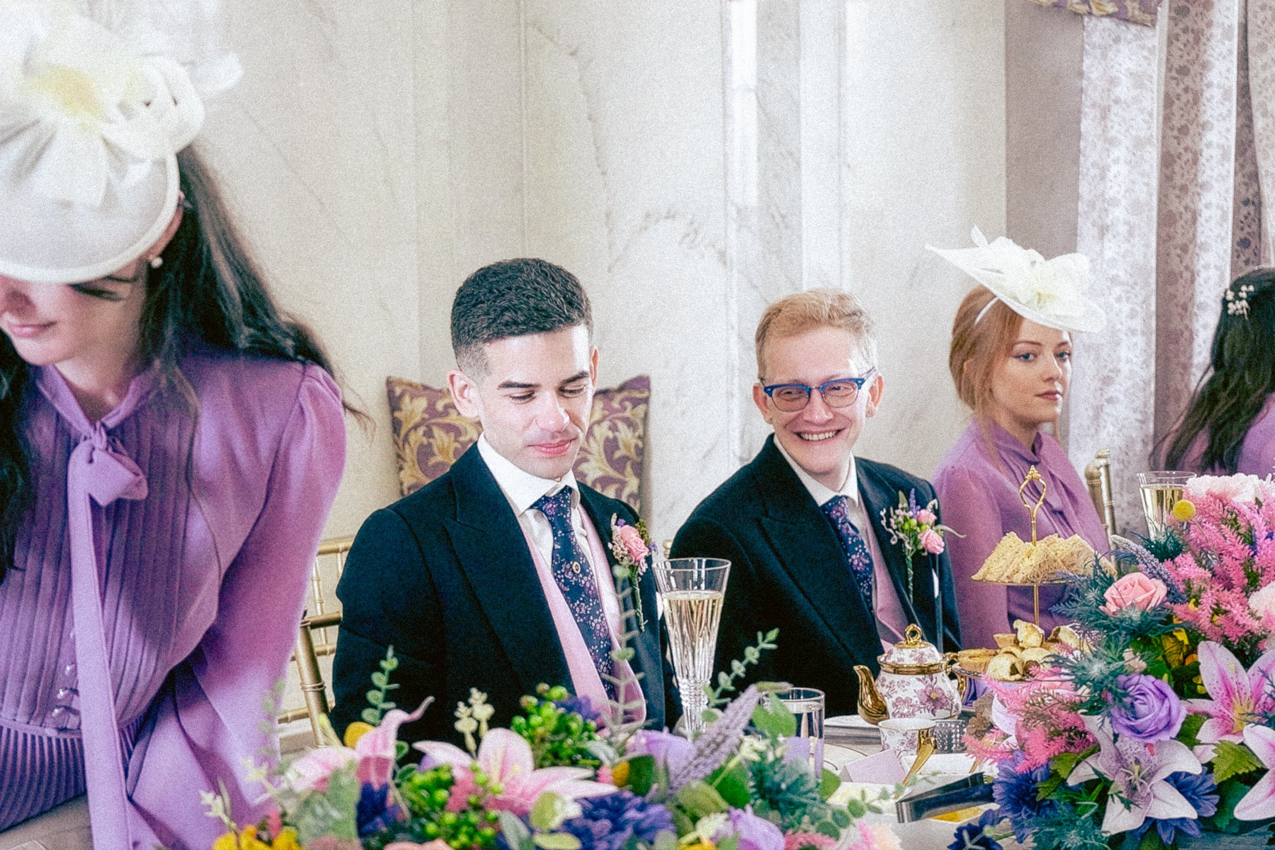 People dressed in formal attire celebrating at a decorated table with colorful flowers, during a special event in an elegant setting.