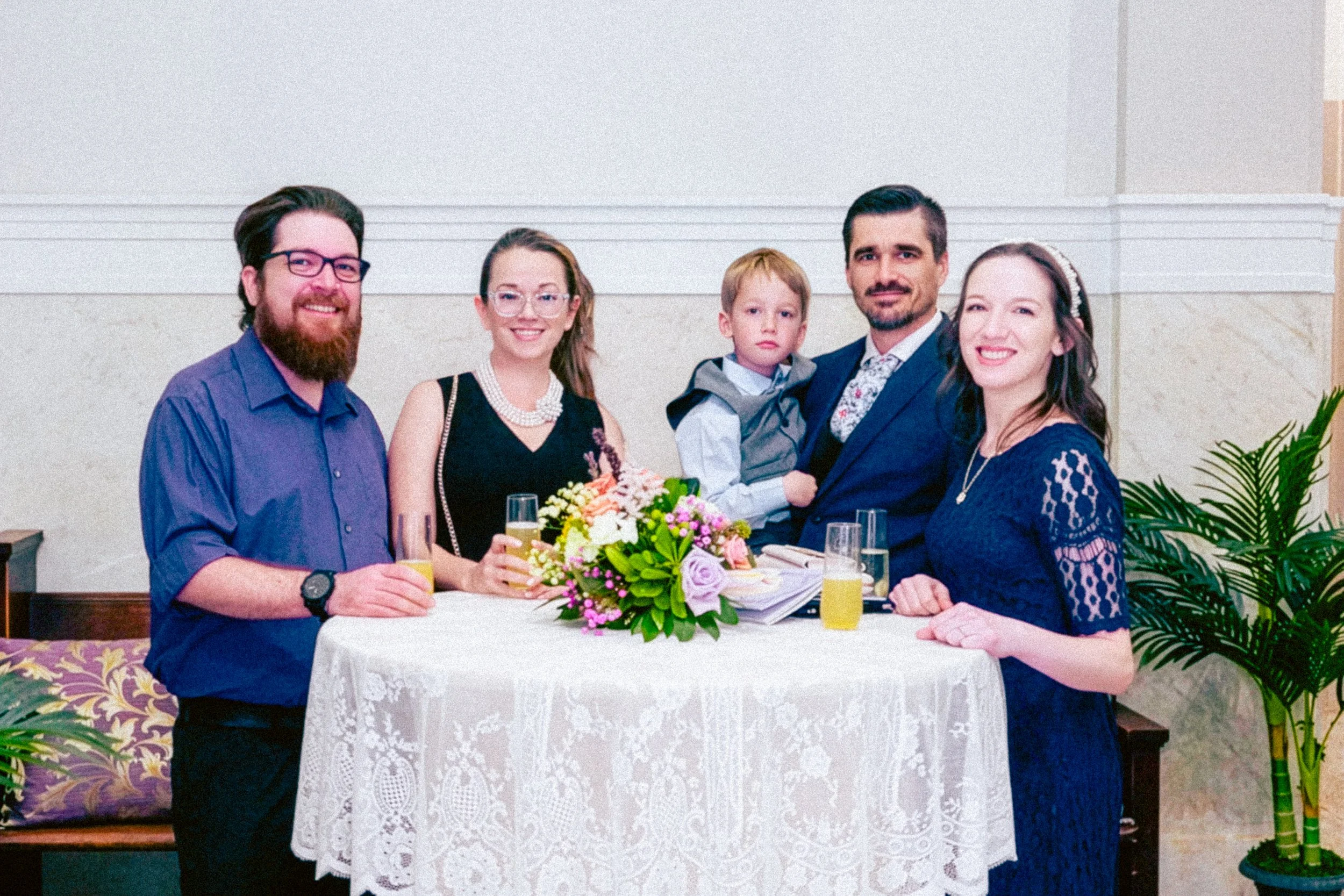 People gathered around a table with a flower centerpiece, celebrating at a social event.