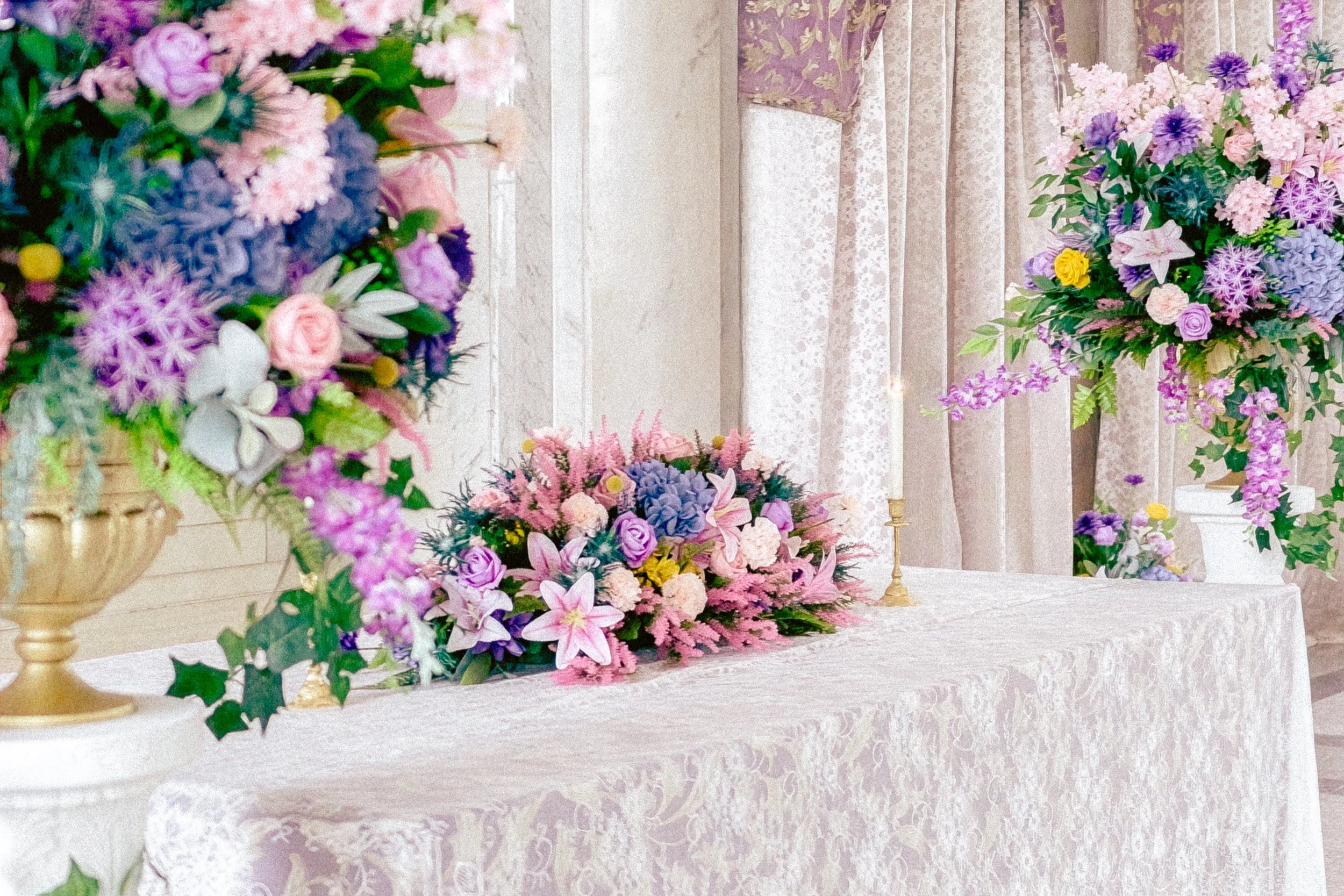 A table decorated with colorful floral arrangements, set against a backdrop of patterned curtains.