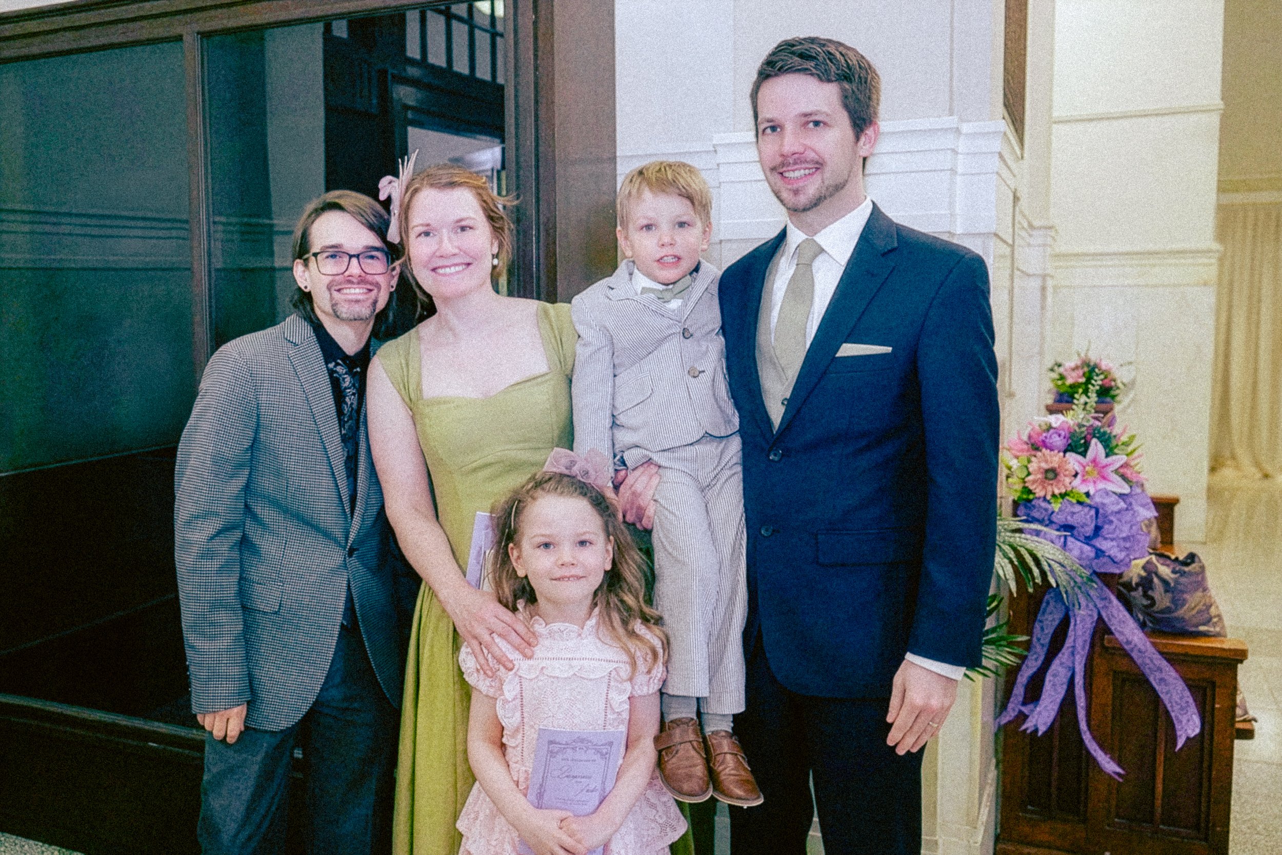 Family photo at a celebration indoors with a floral arrangement banner.