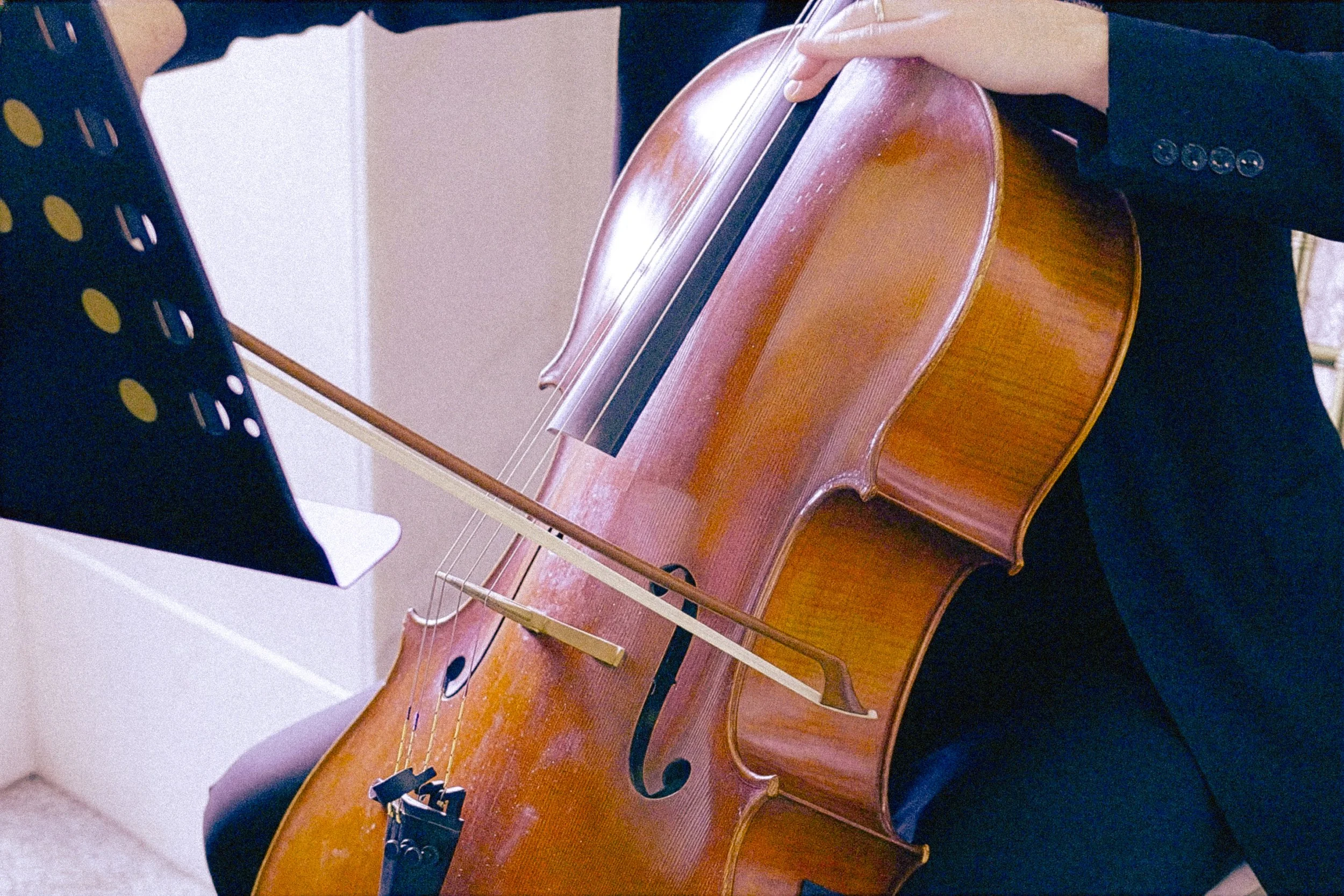 A person playing a wooden cello with a music stand and sheet music in the background.