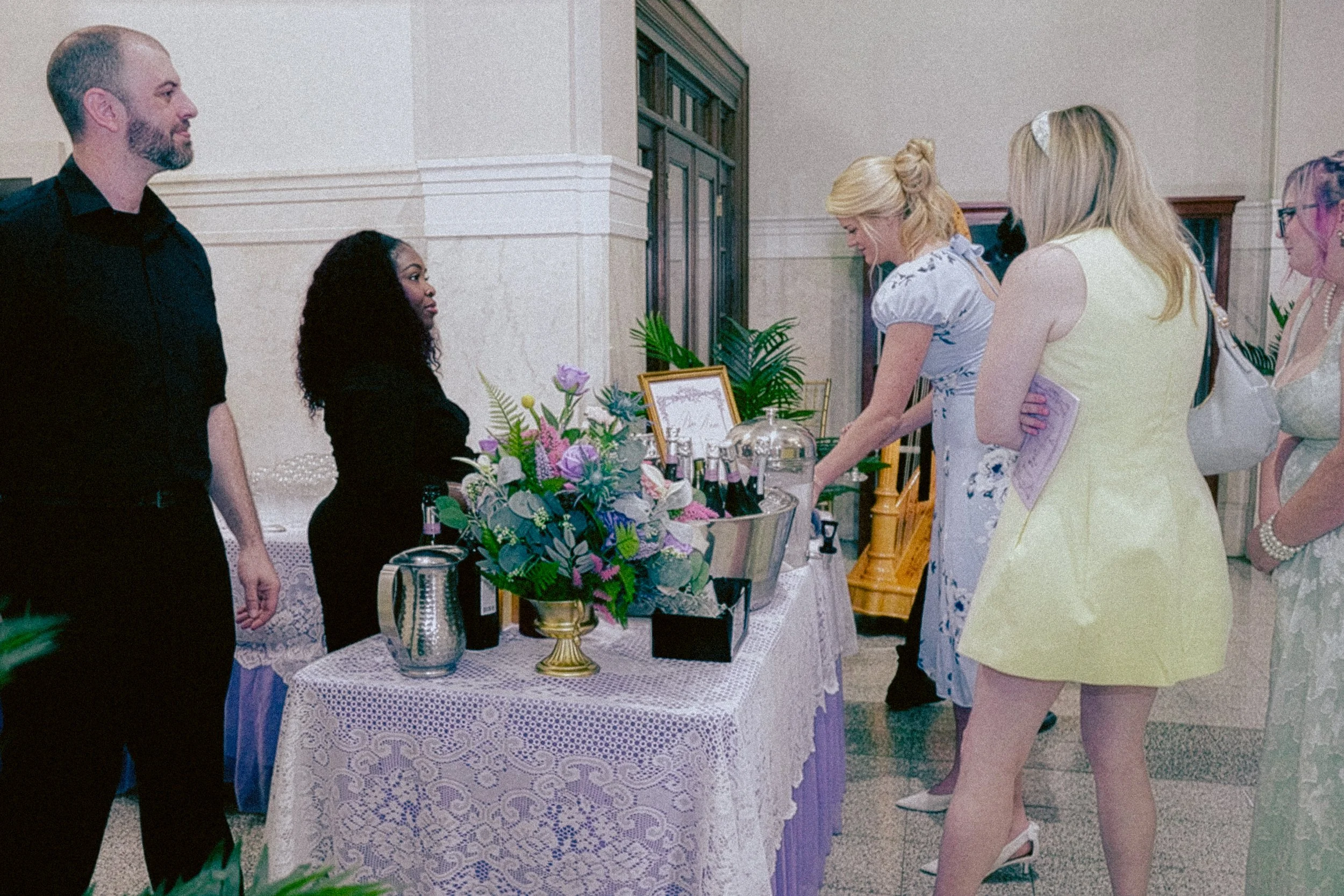 People gathered around a table with floral arrangements and framed items in a room with beige walls and wood paneling.