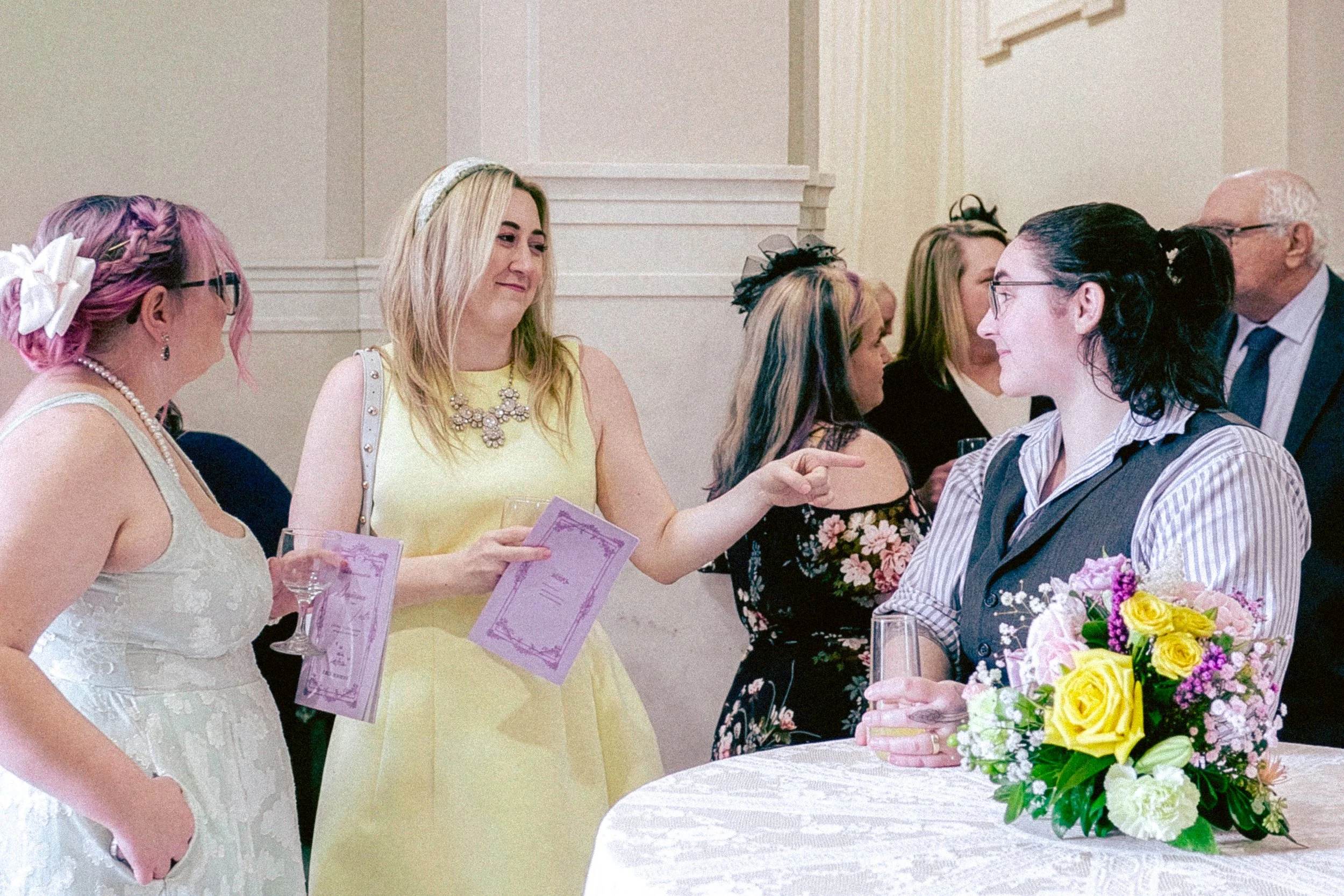 People dressed in colorful outfits exchanging wedding vows near a floral arrangement in a decorated indoor setting.