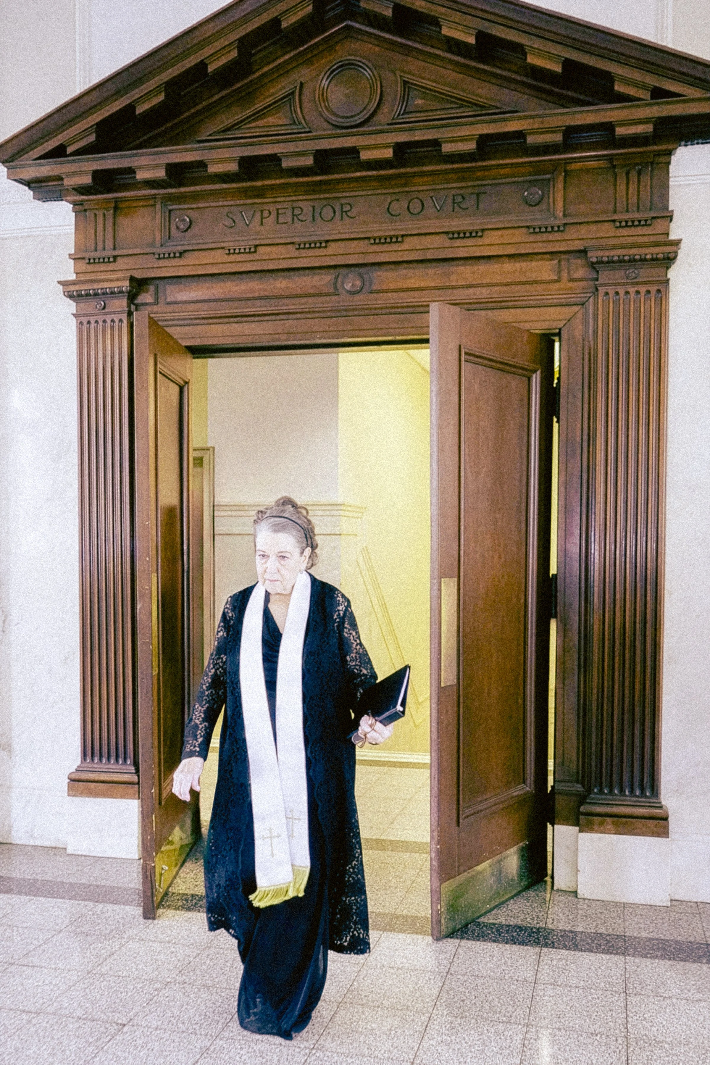 A woman dressed in judicial robes walking through a wooden doorway with a sign above reading 'Superior Court'.