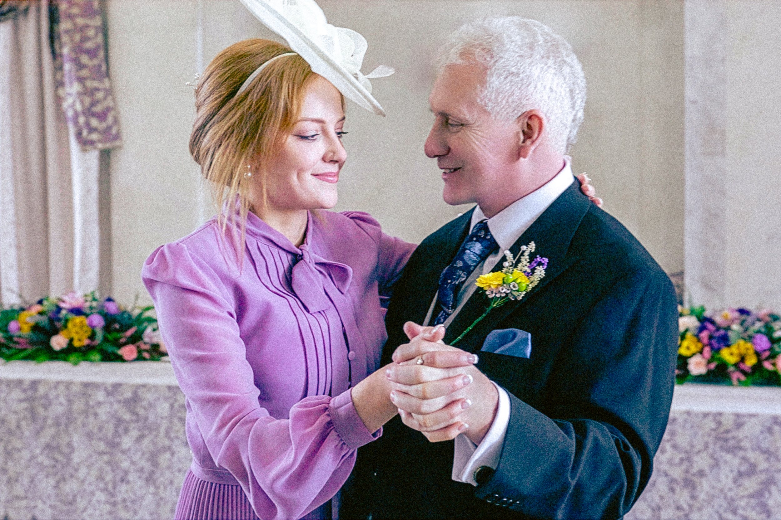 A couple dancing together in a formal setting, with colorful flowers in the background.