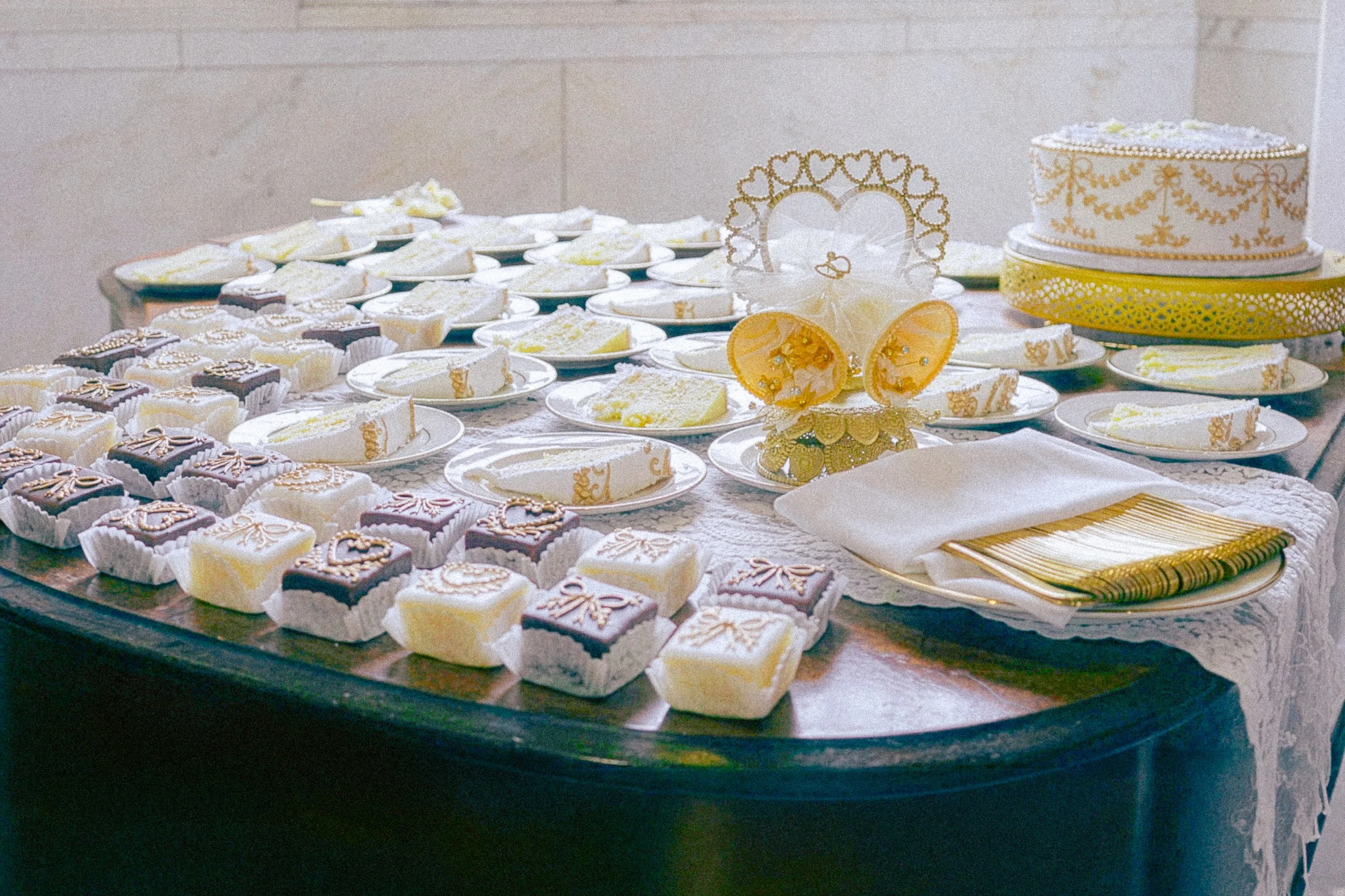 Table filled with assorted decorated cookies and a tiered cake with gold embellishments, likely at a celebration or party.
