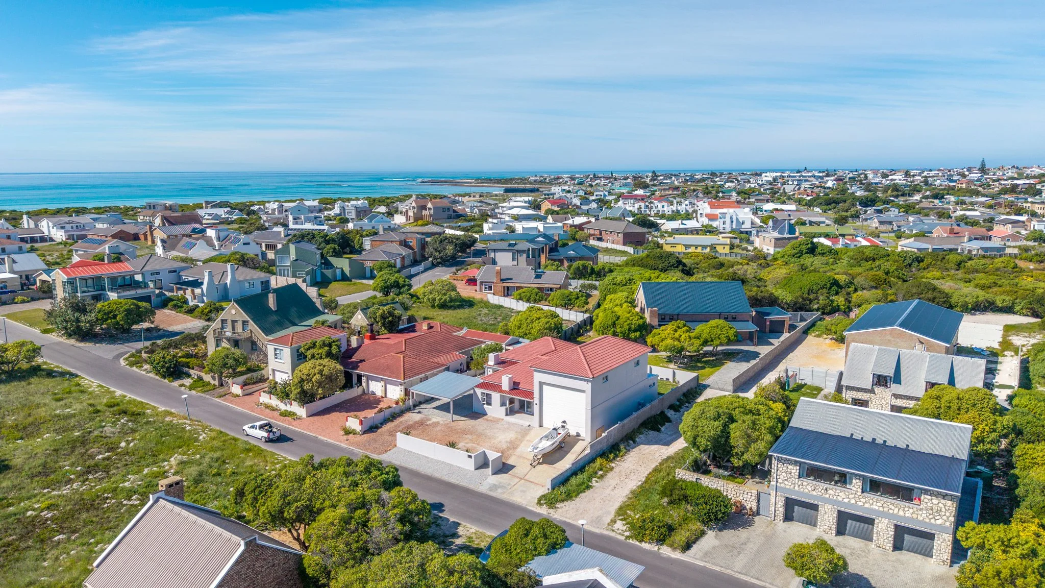 Aerial view of a coastal residential neighborhood with houses, trees, and a view of the ocean in the background.
