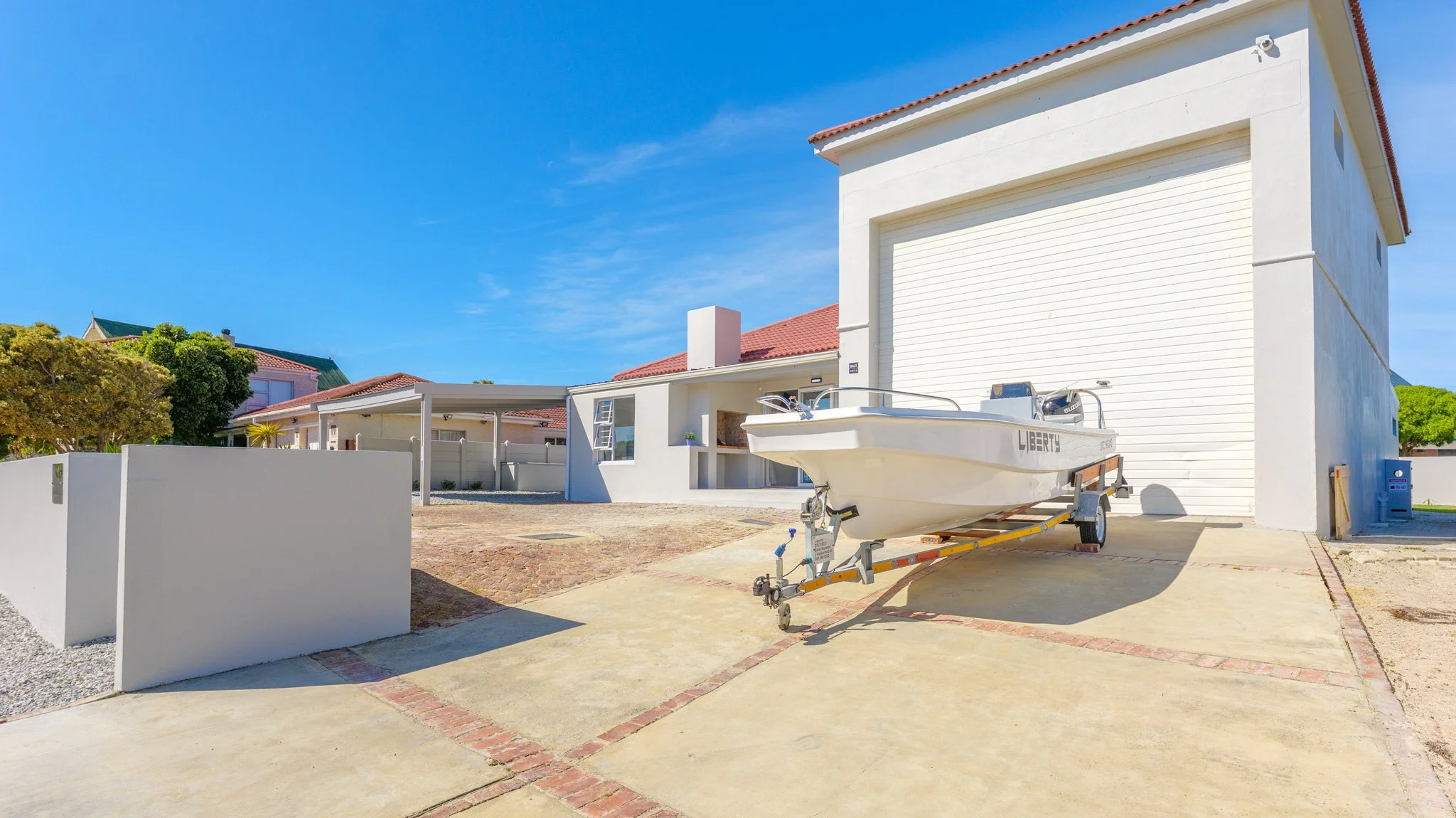 White house with a garage door, boat on a trailer in front, and a blue sky.