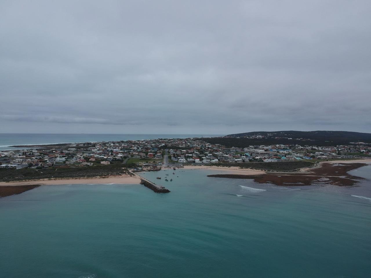 A coastal town with houses, a marina with boats, sandy beaches, and a cloudy sky.